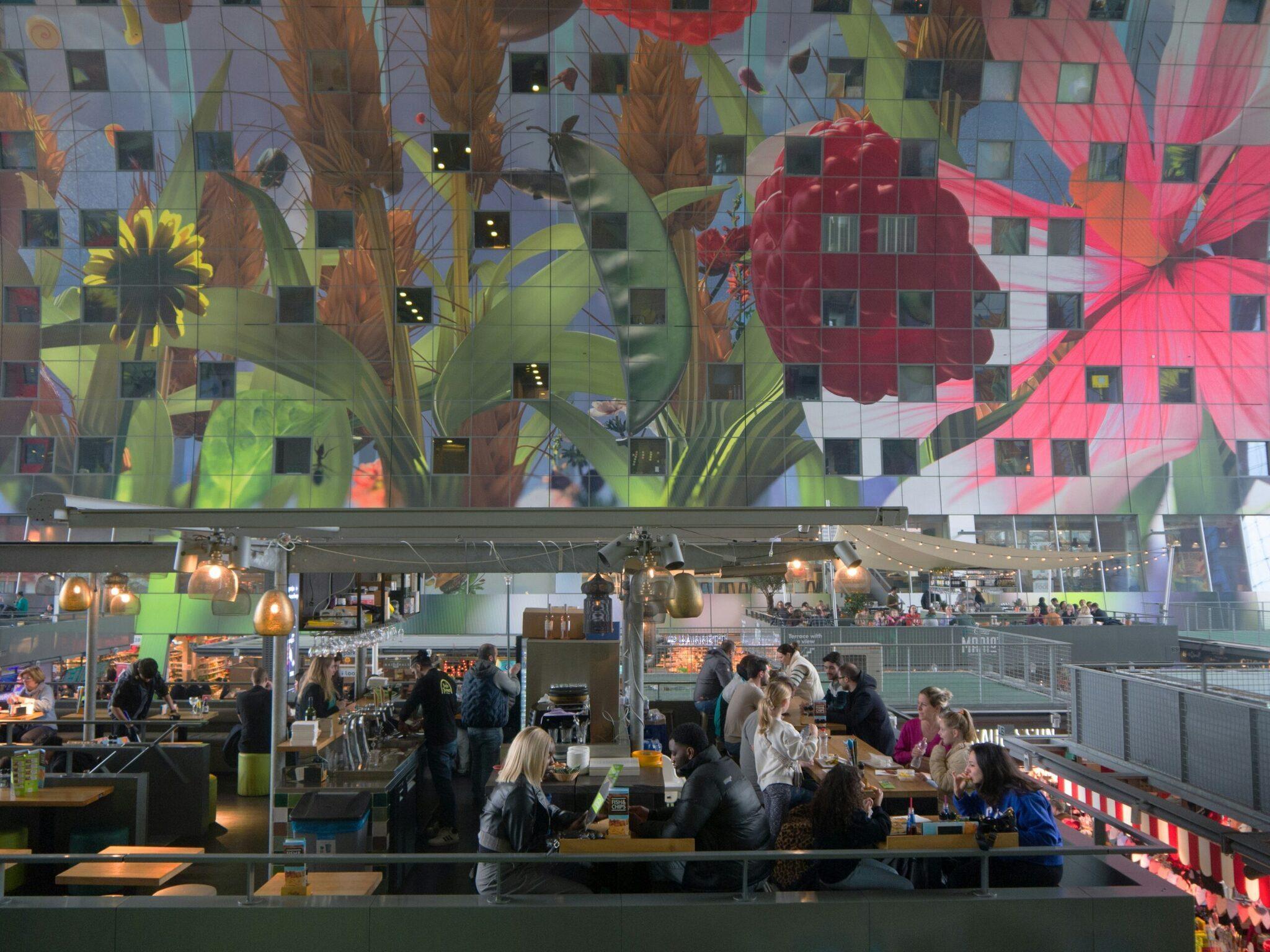 Un marché couvert contemporain avec plafond géant illustré de fleurs colorées, visiteurs et étals de restauration