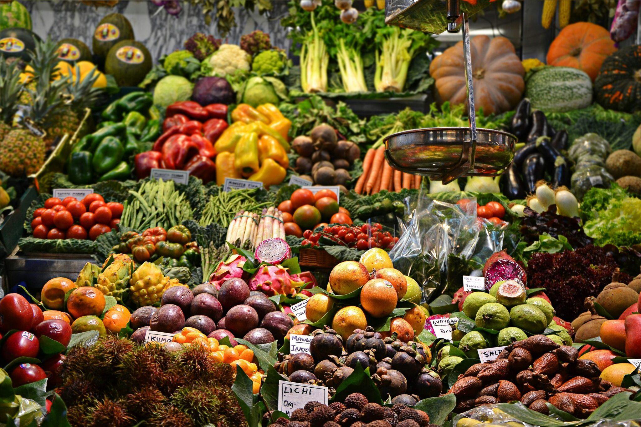 Un étal de marché coloré présentant fruits et légumes frais avec un filet d’eau versée en avant-plan