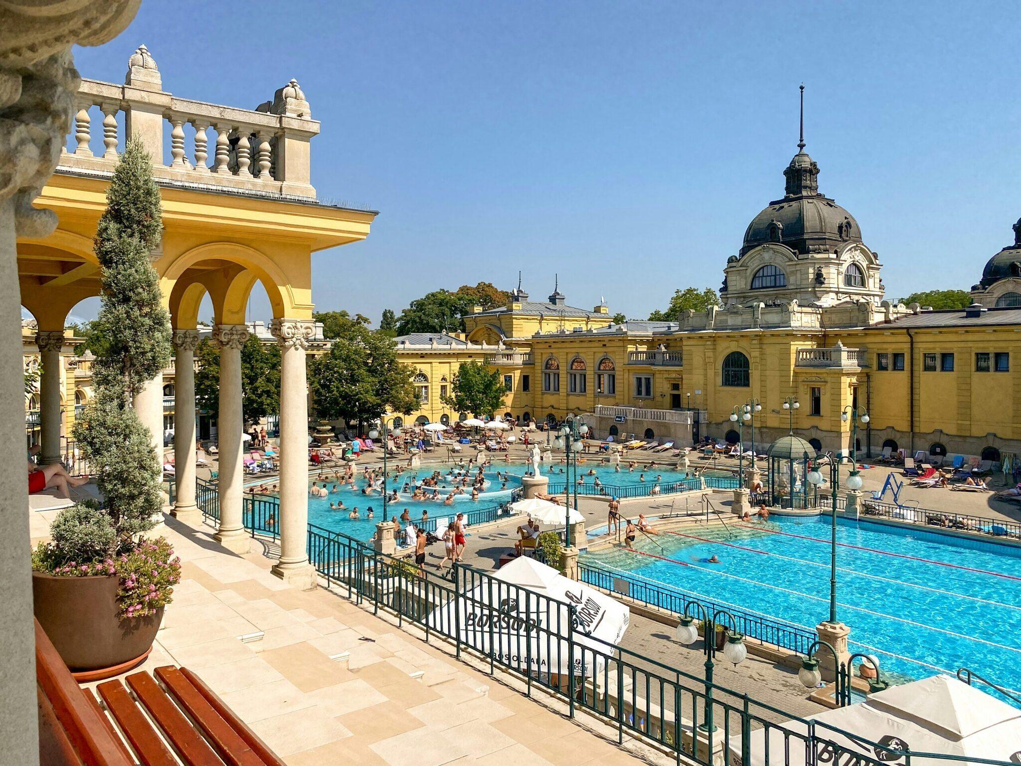 Vue panoramique des bains thermaux avec piscines turquoise, architecture jaune et dôme, baigneurs détendus par beau temps