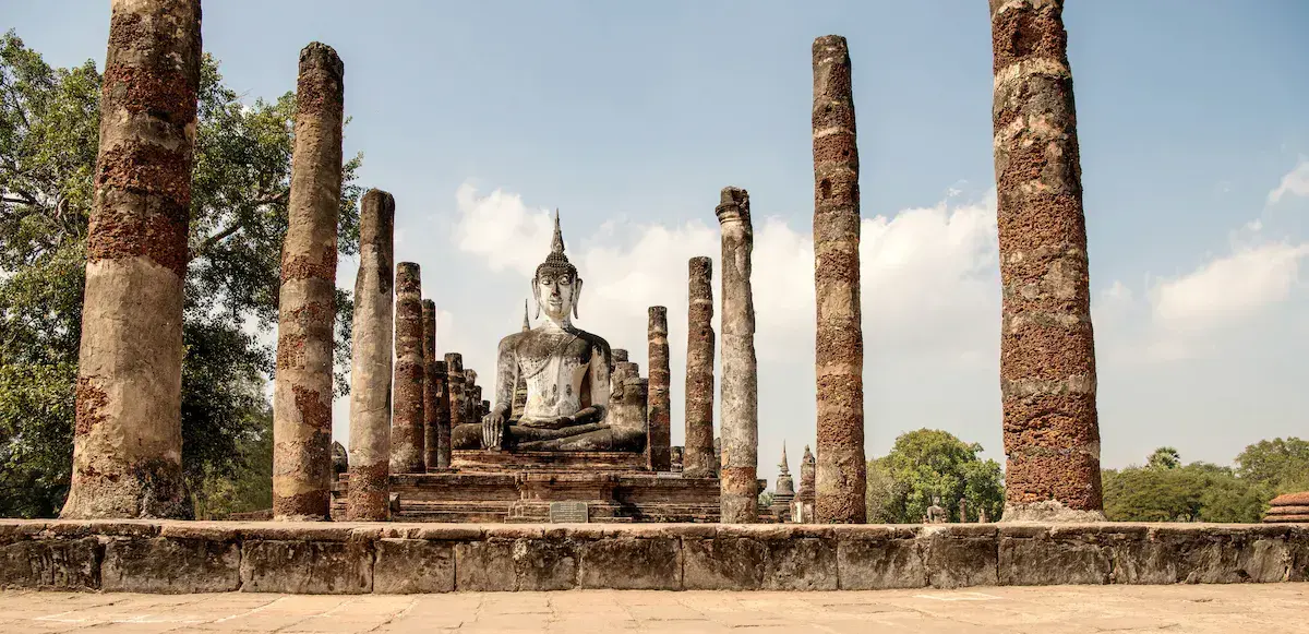 Statue de Bouddha assis entourée de colonnes de pierre dans les ruines d’un ancien temple thaïlandais