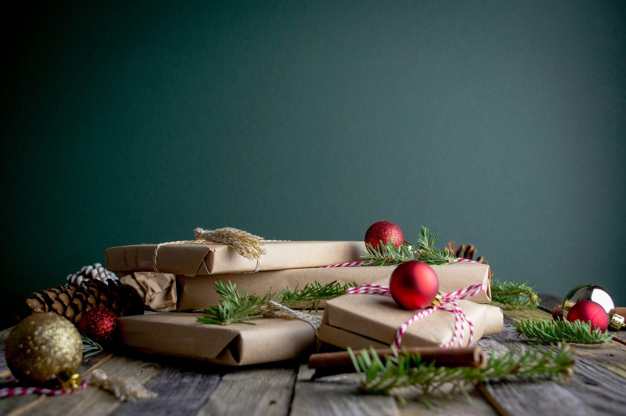 Composition de cadeaux enveloppés kraft avec rubans rose et blanc, décorée de boules rouges, sapin et pommes de pin sur bois