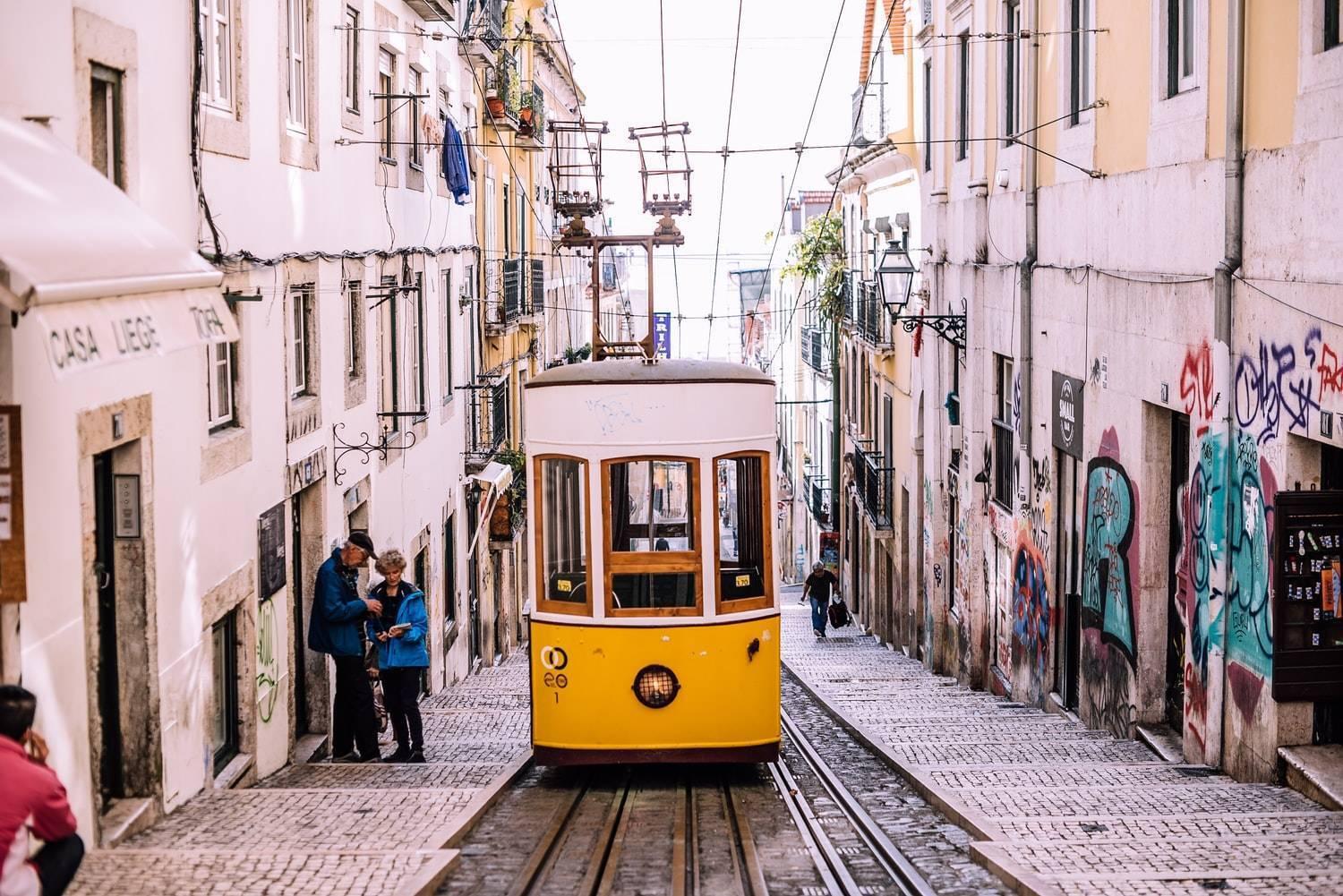 Un tramway jaune historique grimpe une rue pavée étroite bordée de bâtiments colorés dans une ville européenne