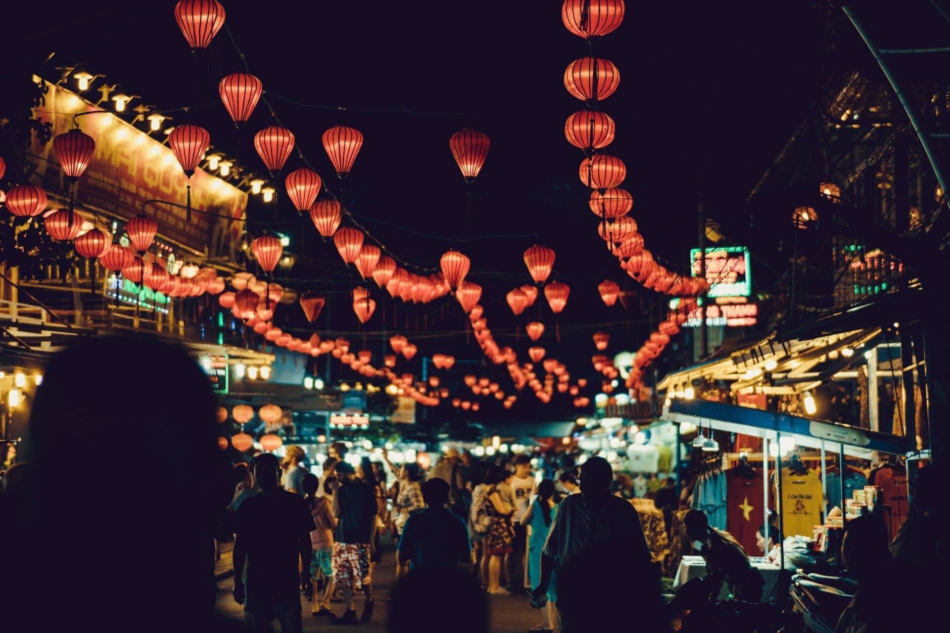 Une rue commerçante animée la nuit, illuminée par des lanternes rouges traditionnelles et des façades lumineuses
