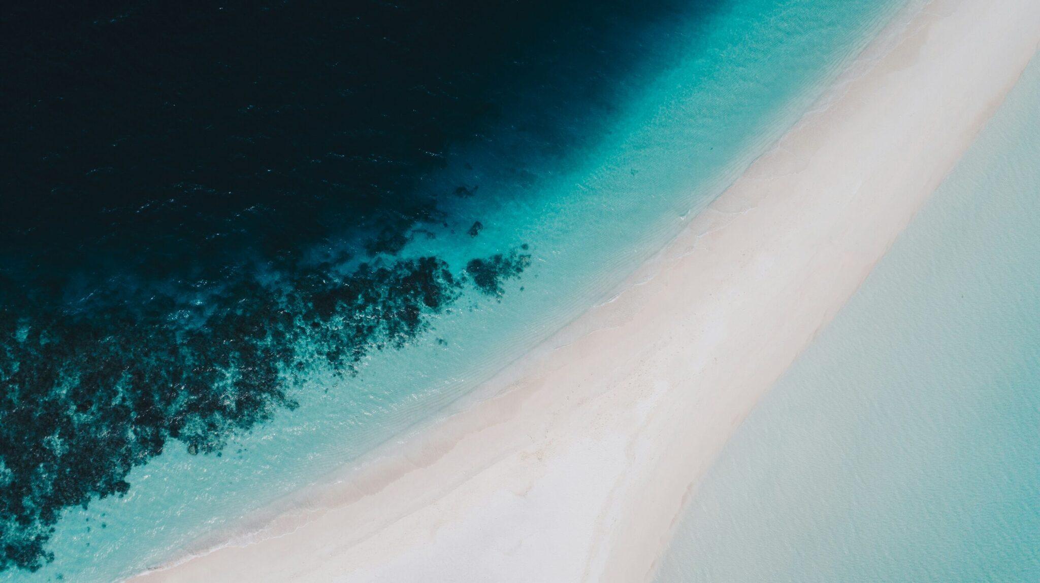 Vue aérienne d’une plage de sable blanc bordée par un récif corallien aux eaux turquoise dégradées