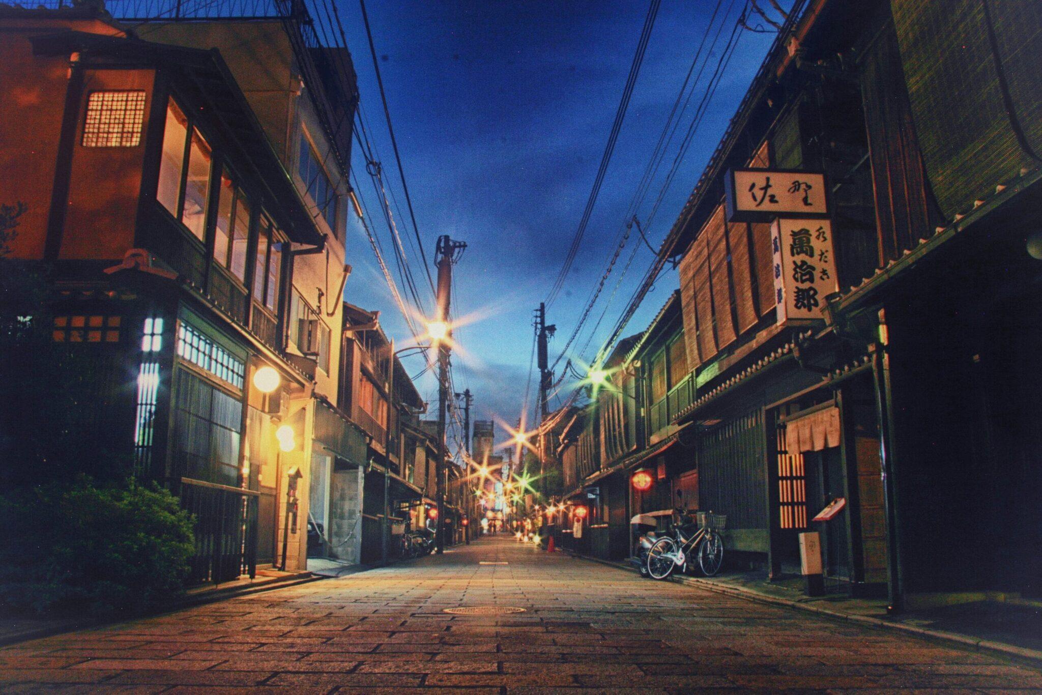 Une ruelle historique japonaise illuminée le soir avec maisons traditionnelles, lanternes et signalétique asiatique