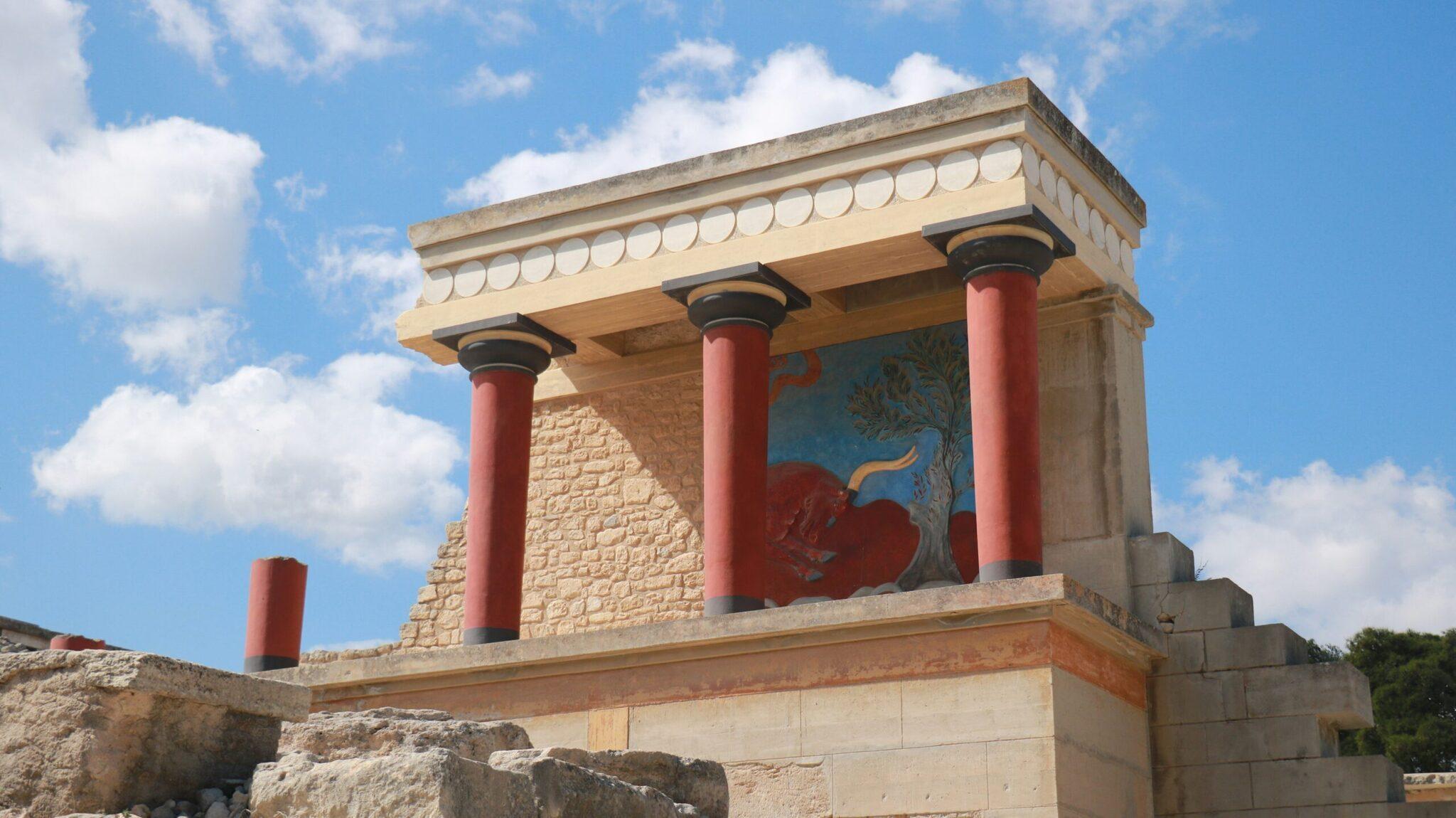 Reconstitution d’un palais minoen antique avec colonnes rouges et fresques murales colorées sous un ciel dégagé