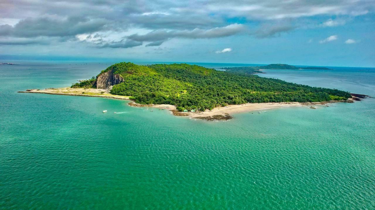 Une île tropicale densément boisée entourée d’eaux turquoise avec plages de sable blanc et rochers côtiers