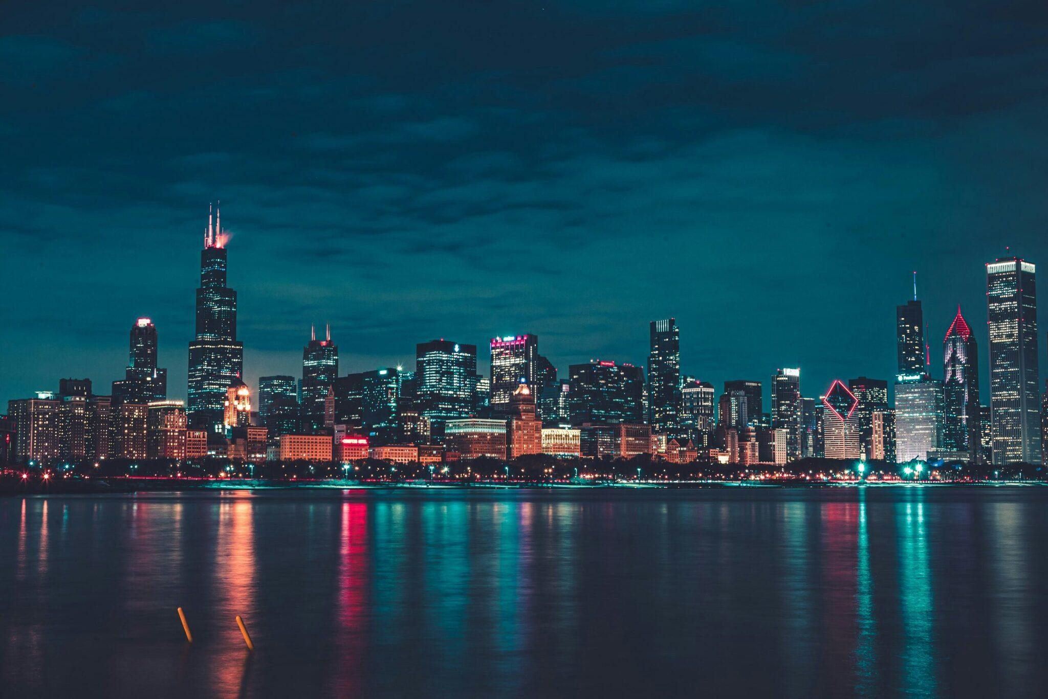 Skyline urbain illuminé la nuit avec gratte-ciel reflétés dans l’eau calme d’un lac ou fleuve