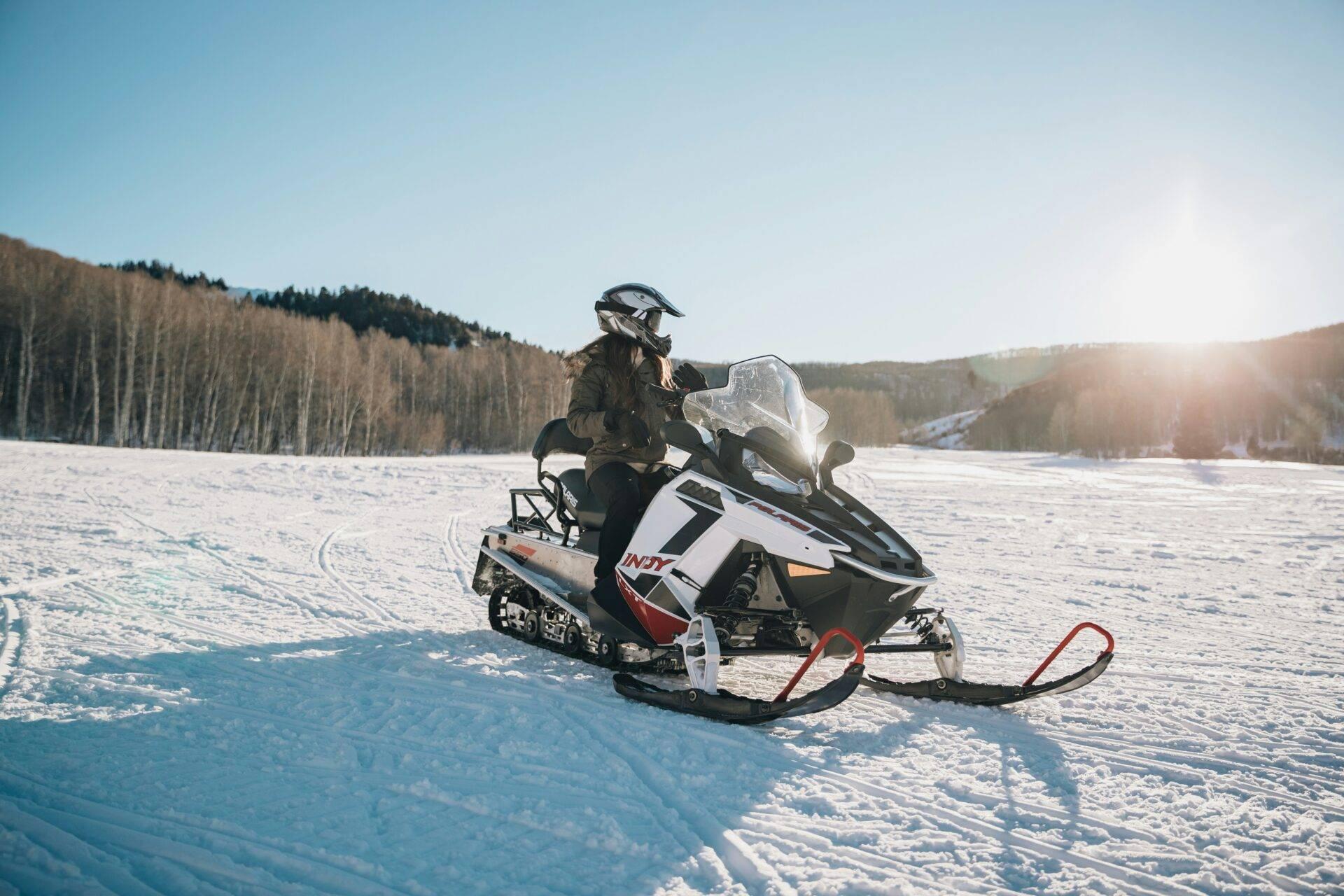 Un motoneigiste en tenue d’hiver traverse un lac gelé entouré de forêts de conifères enneigées