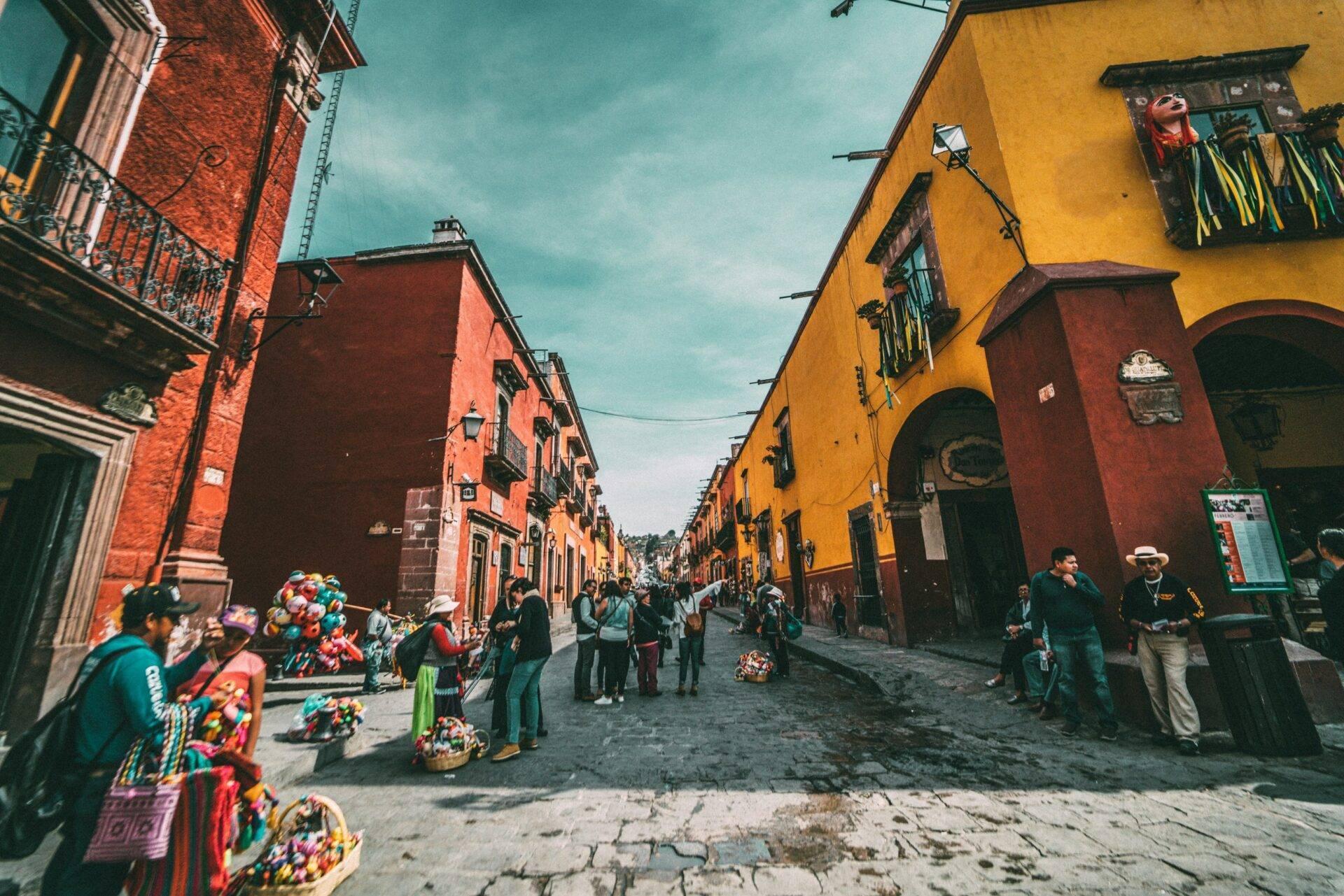 Une rue coloniale colorée avec des bâtiments rouge et jaune, des vendeurs ambulants et des touristes sous un ciel bleu