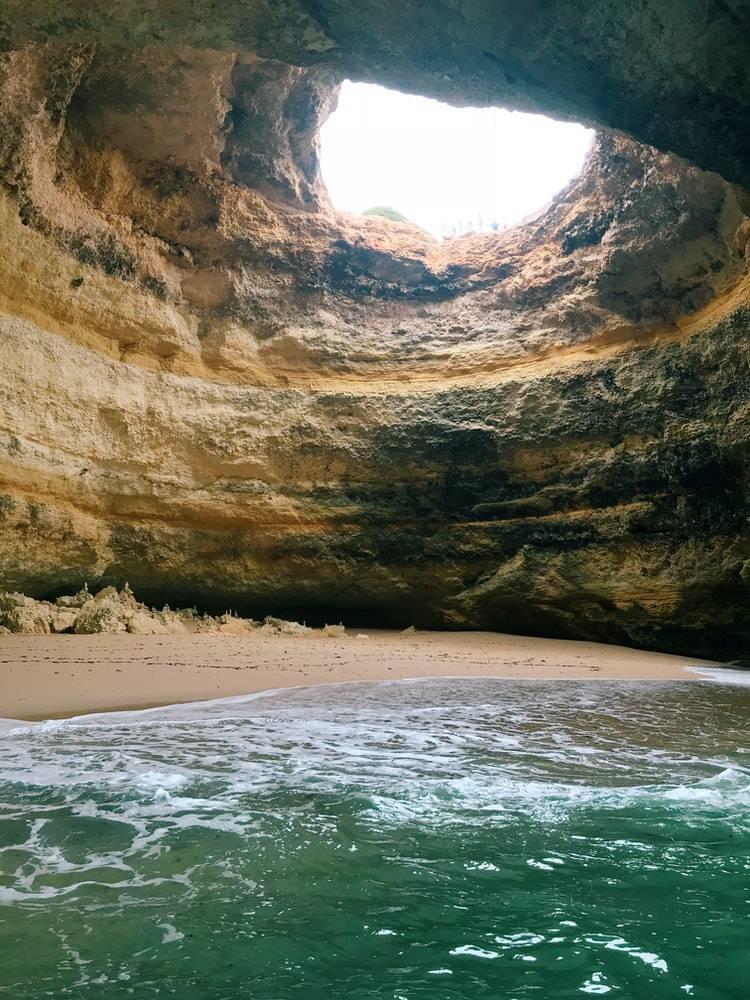 Une grotte côtière impressionnante avec ouverture naturelle en voûte surplombant une plage et l’océan