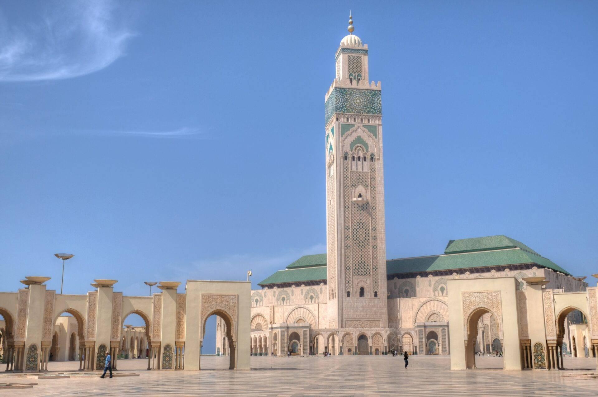 Grande mosquée avec minaret blanc élancé et cour pavée sous ciel bleu dégagé