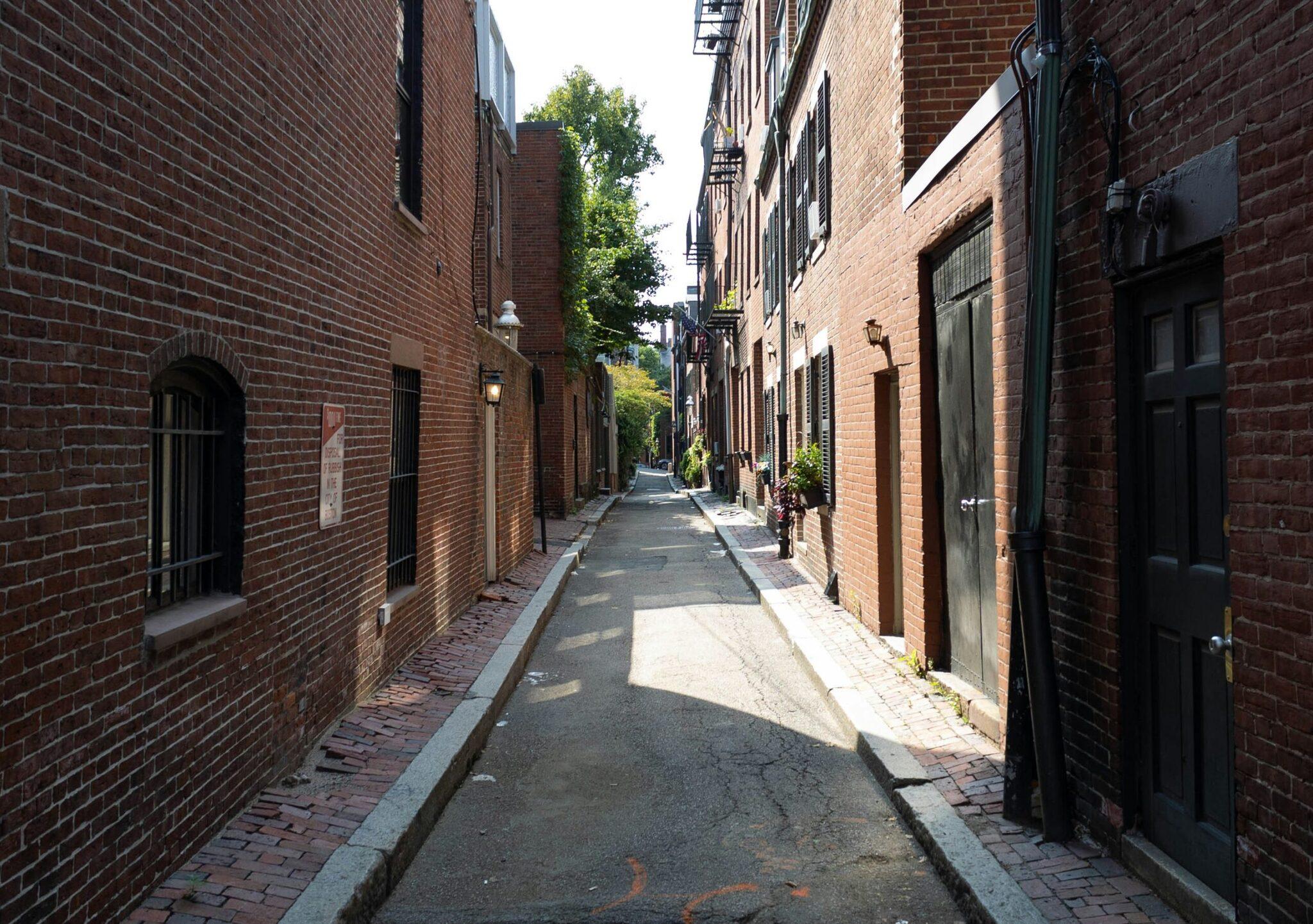 Une ruelle pavée historique bordée de briques rouges avec portes vertes et bâtiments anciens