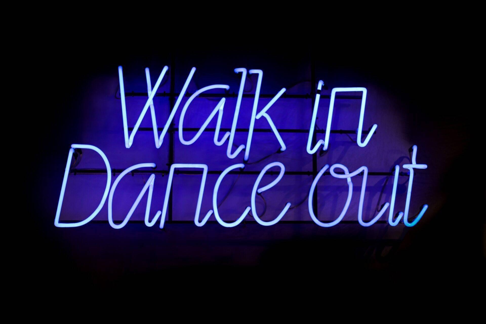 Enseigne lumineuse en néon bleu affichant “Walk in Danceout” sur fond sombre, ambiance urbaine de vie nocturne