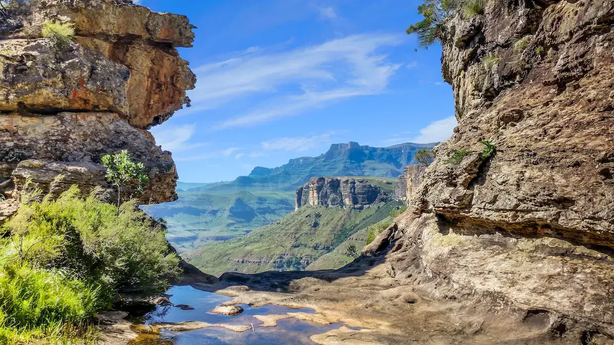 Vue depuis une grotte rocheuse sur des montagnes escarpées et verdoyantes avec un petit lac en contrebas