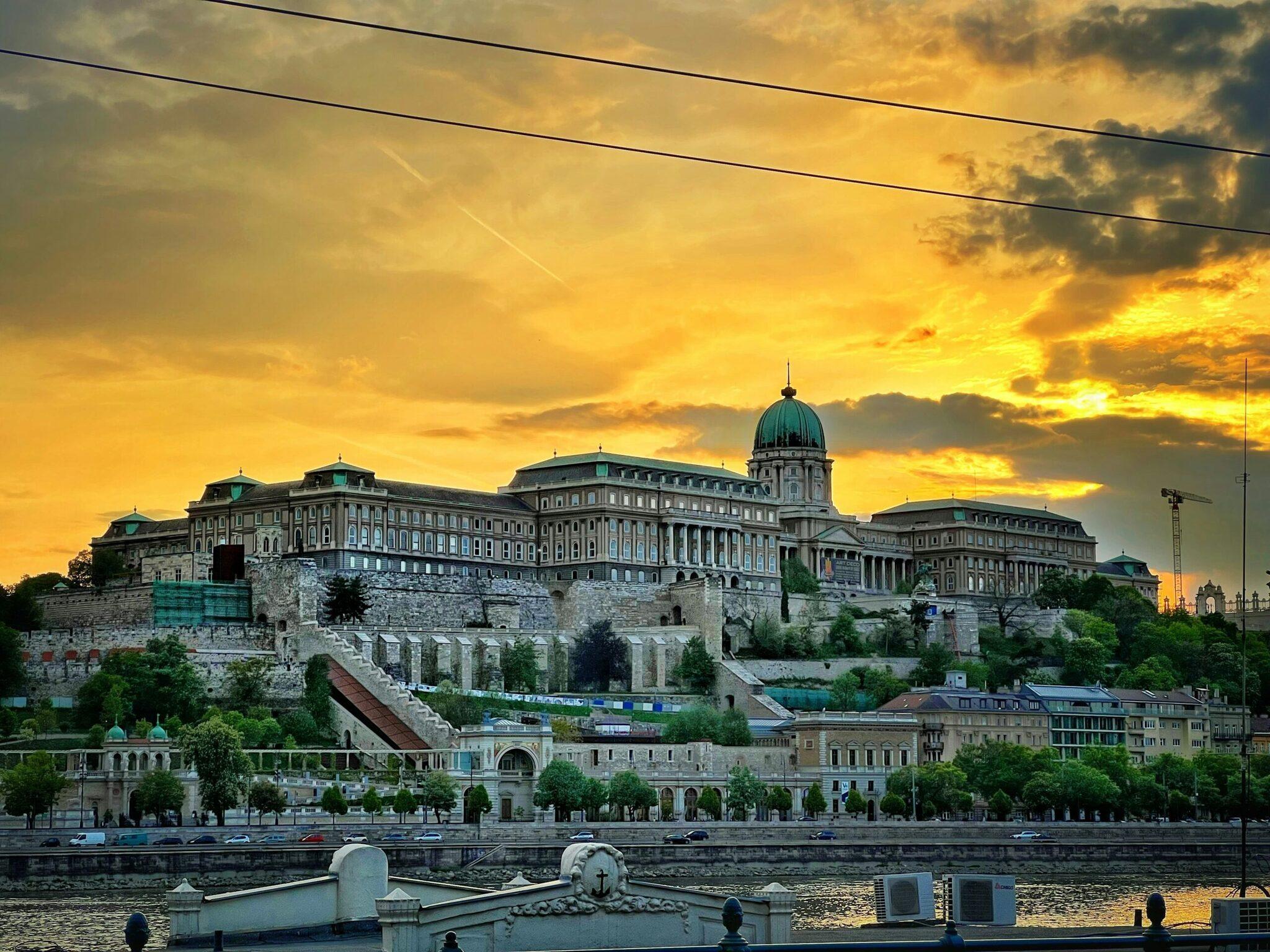 Le Château de Buda surplombe le Danube au coucher de soleil doré, avec ses façades historiques et son dôme emblématique