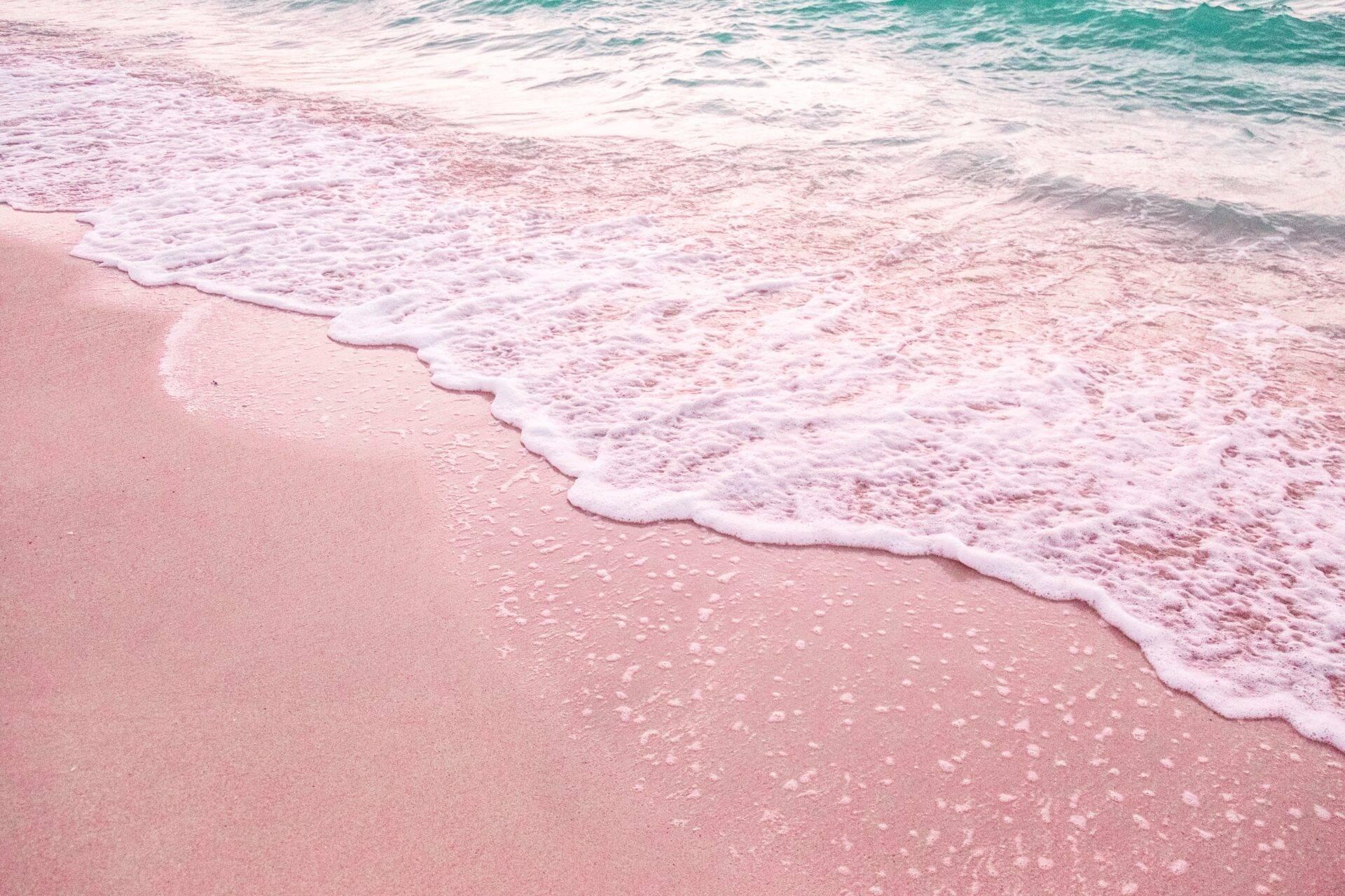 Plage de sable rose avec vagues turquoise et mousse blanche, créant une atmosphère tropicale paradisiaque