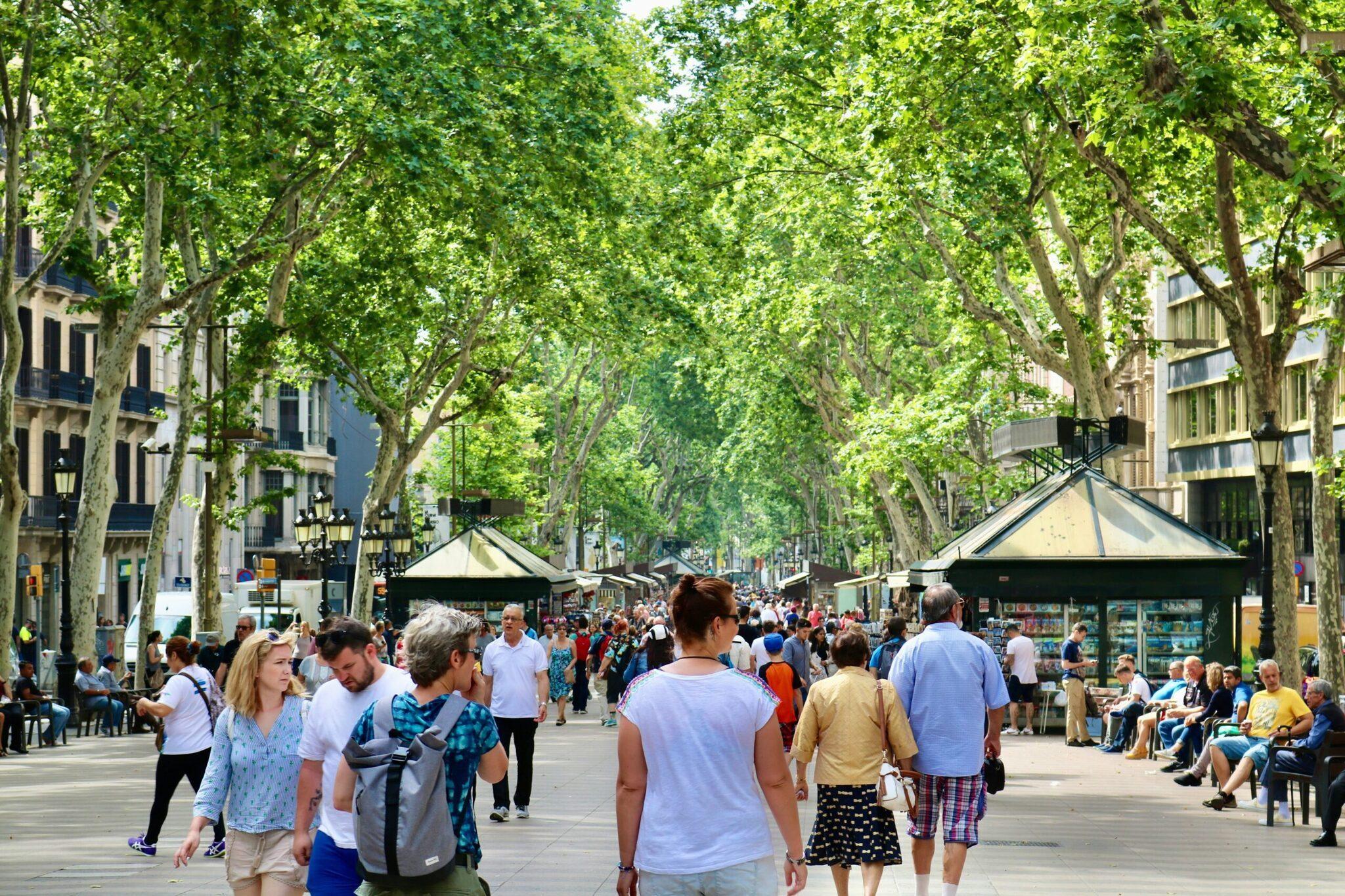 Une rue piétonne bordée d’arbres avec foule de touristes, boutiques et terrasses de café en milieu urbain