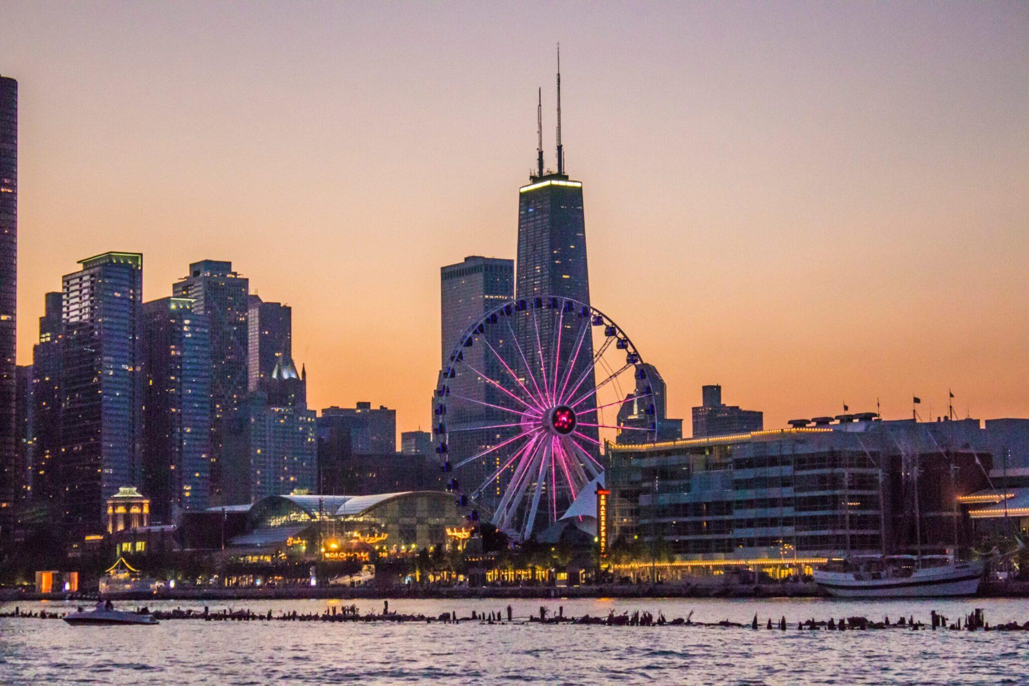 Skyline urbain au coucher de soleil avec grande roue illuminée en rose et gratte-ciel en arrière-plan au bord de l’eau