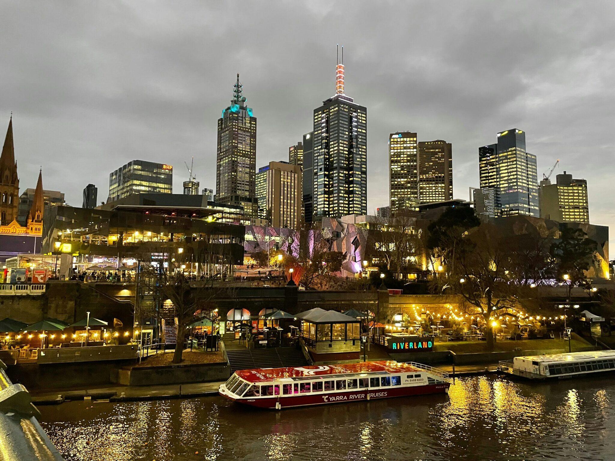 Skyline urbain illuminé au crépuscule avec gratte-ciel, bateau touristique sur la rivière et zone riveraine aménagée