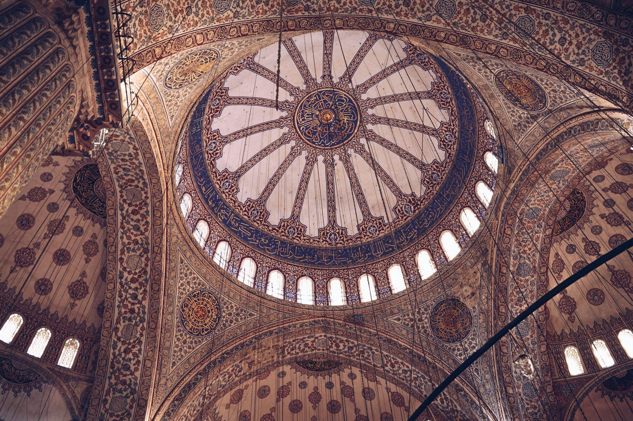 Intérieur d’une mosquée avec dôme central orné de motifs géométriques et calligraphie islamique, lumière naturelle des fenêtres