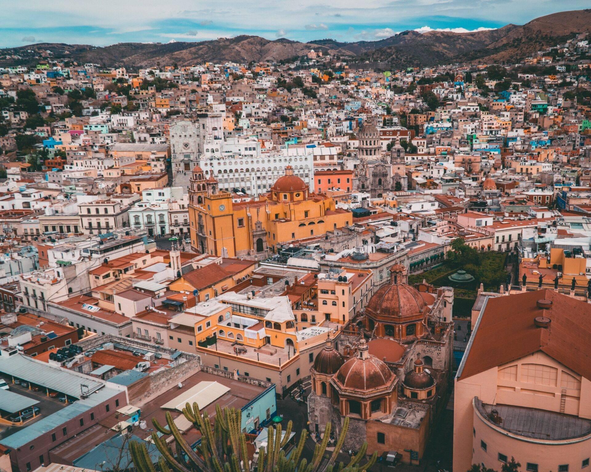 Vue aérienne d’une ville coloniale mexicaine avec églises aux dômes ocre, architecture colorée et montagnes boisées