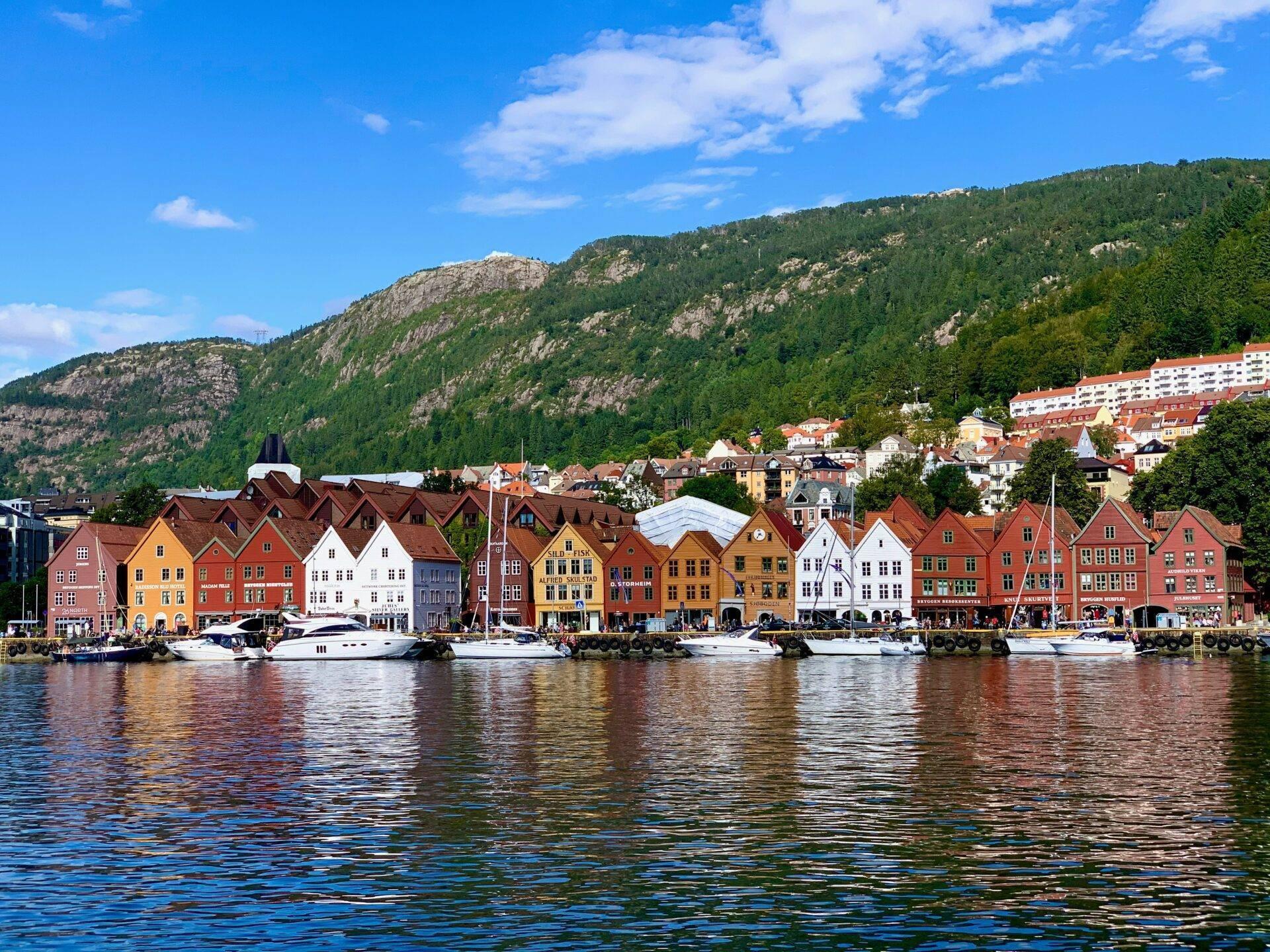Rangée de maisons colorées au bord d’un fjord norvégien avec montagnes boisées en arrière-plan