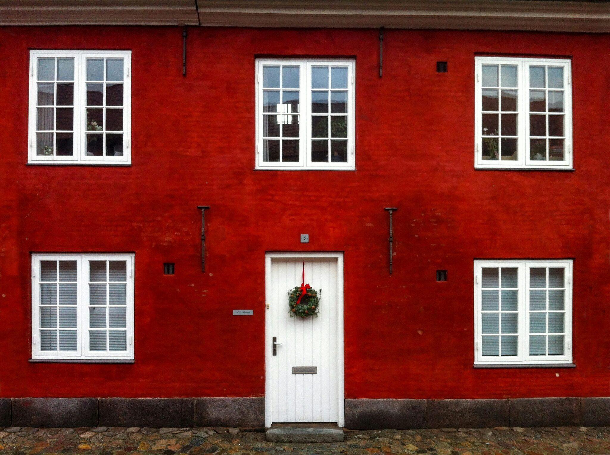 Façade rouge éclatante d’une maison traditionnelle scandivage avec porte blanche décorée d’une couronne de Noël