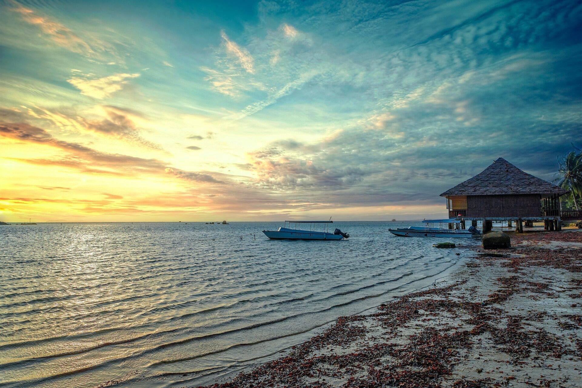 Un coucher de soleil tropical sur une plage de sable avec bungalow sur pilotis et bateaux de pêche ancrés