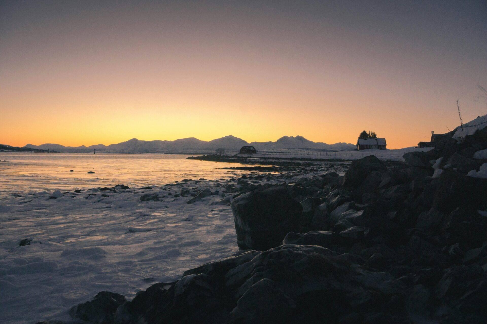 Coucher de soleil sur une côte rocheuse avec bâtiments côtiers et montagnes en arrière-plan