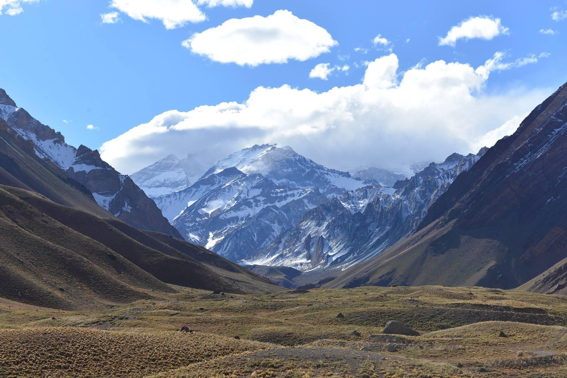 Vallée de montagne enneigée encadrée par des pics rocheux arides sous un ciel bleu dégagé