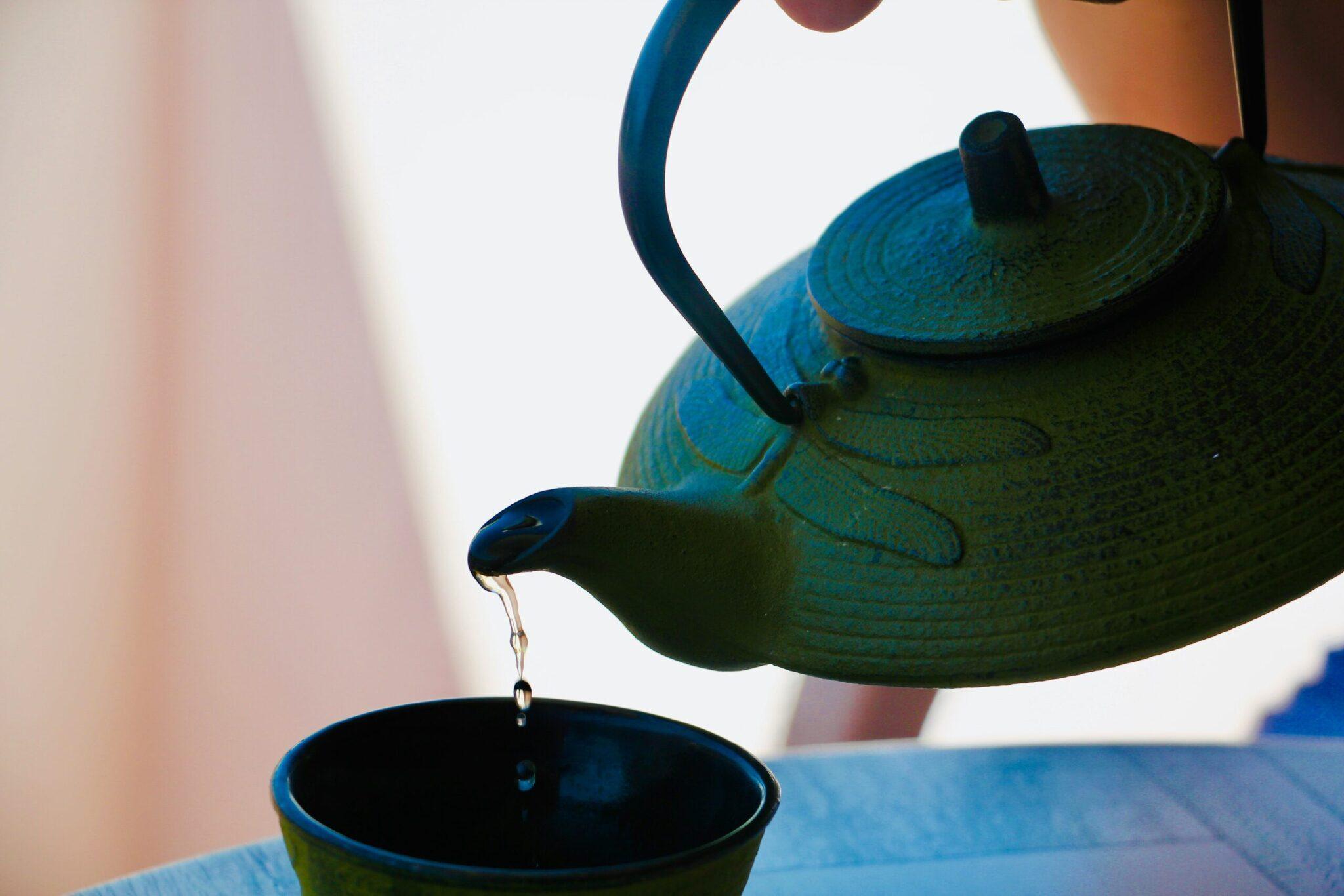 Une théière bleue en fonte asiatique verse du thé chaud dans une tasse, illustrant une pause culturelle lors d’un voyage