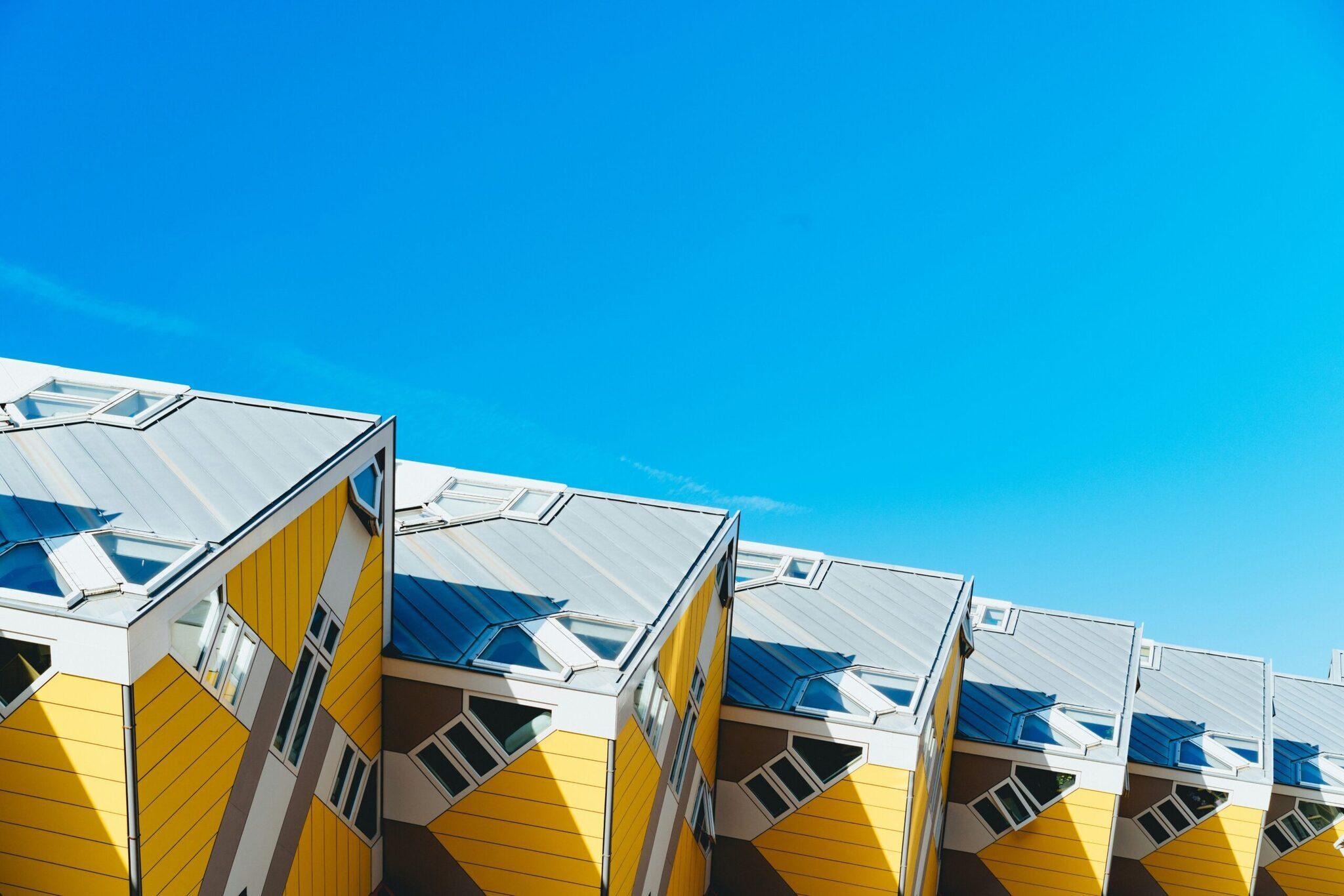 Maisons cubiques jaunes et blanches avec toits bleus sous un ciel dégagé, architecture moderne emblématique