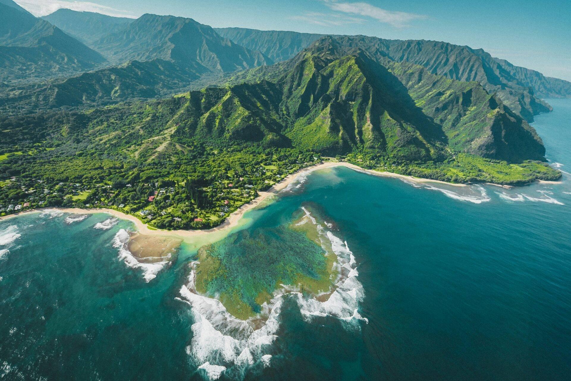 Vue aérienne d’une vallée côtière tropicale avec falaises verdoyantes, plages de sable et océan turquoise sous ciel dégagé