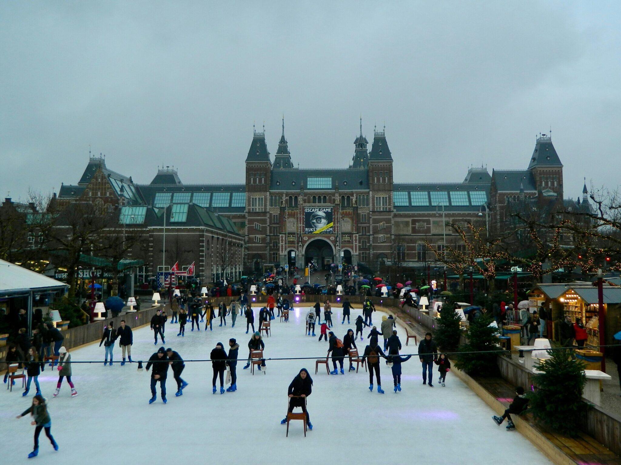 Patinoire extérieure animée devant un imposant bâtiment historique aux toits verts et tourelles, entourée de décors festifs