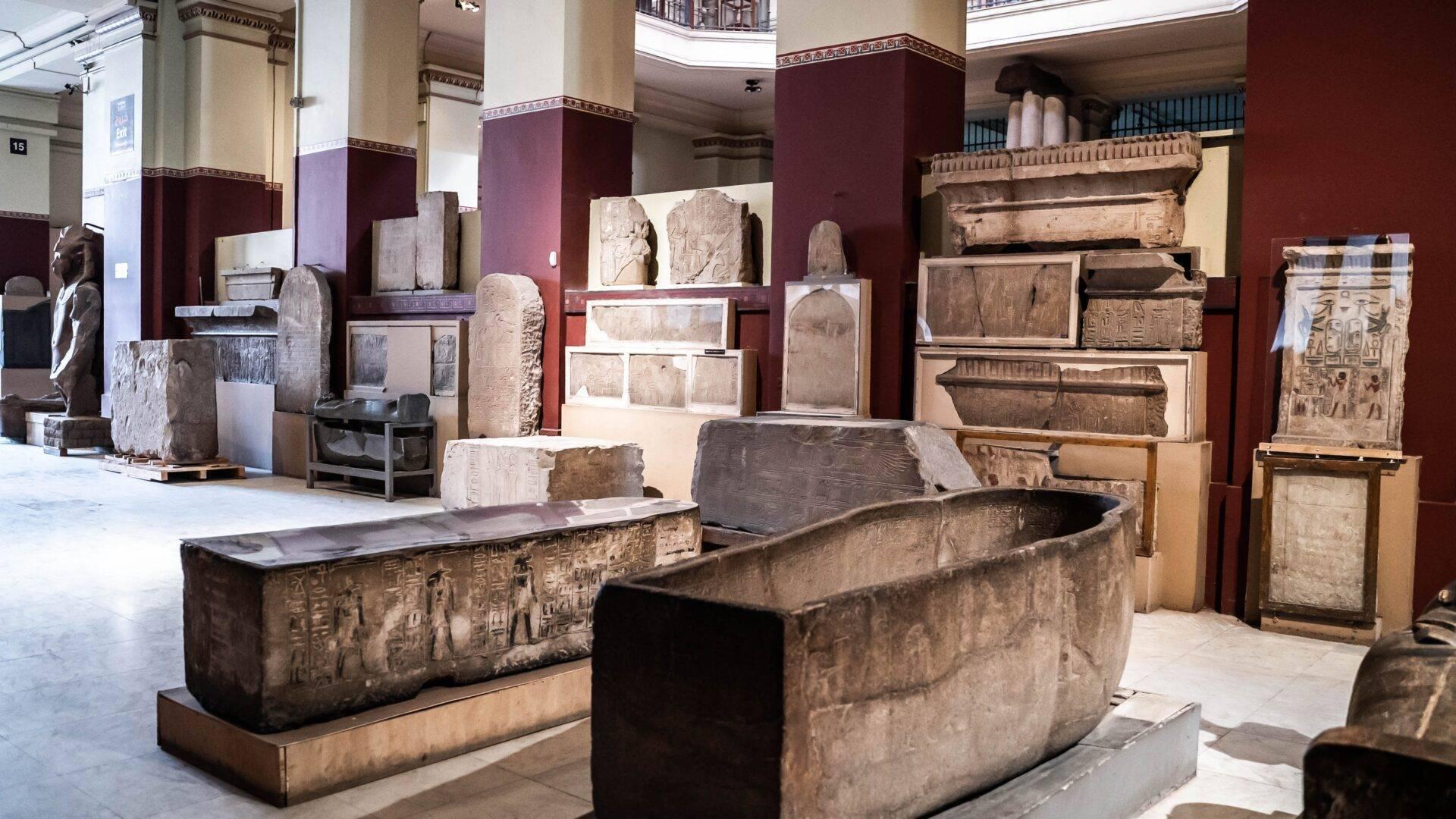 Sarcophages égyptiens antiques et bas-reliefs exposés dans une galerie de musée aux murs bordeaux