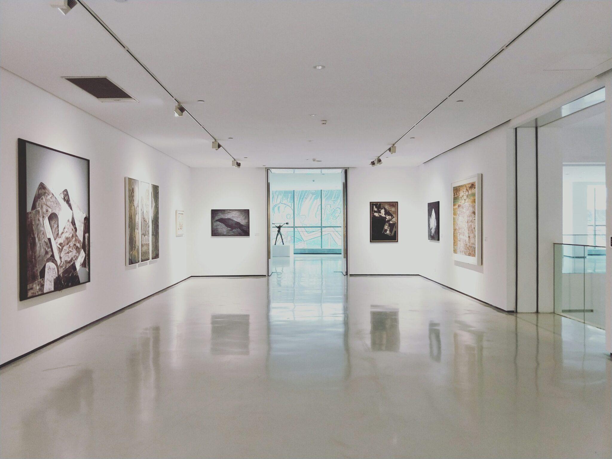 Galerie d’art moderne avec exposition photographique, sol blanc brillant et baies vitrées panoramiques sur la ville