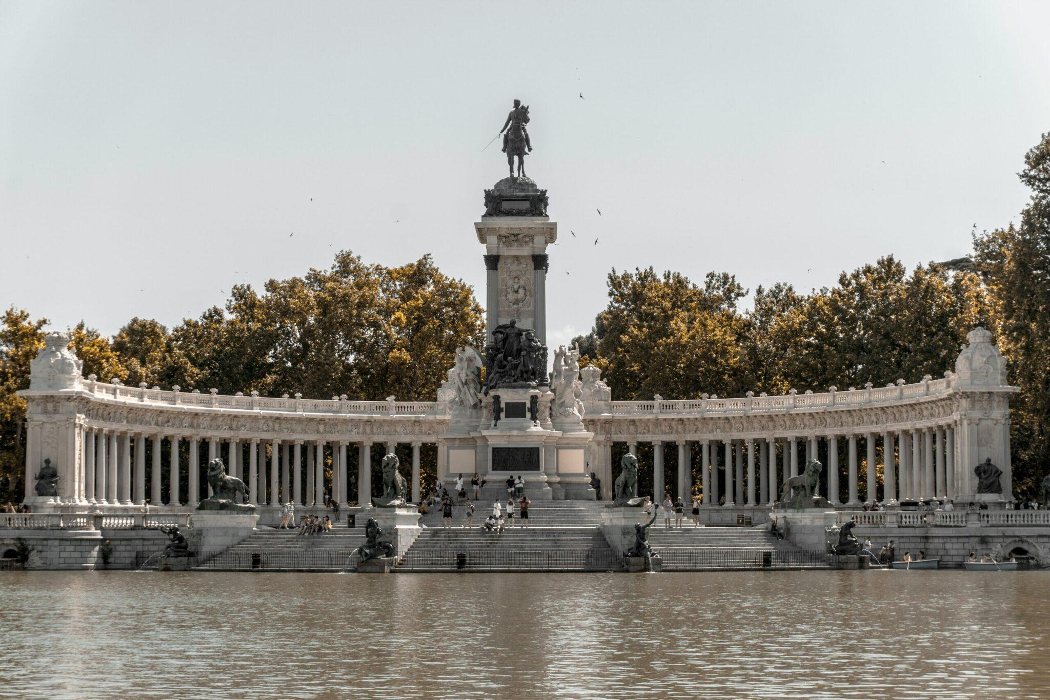 Monument avec colonnade blanche et statue équestre surplombant un plan d’eau, entouré d’arbres