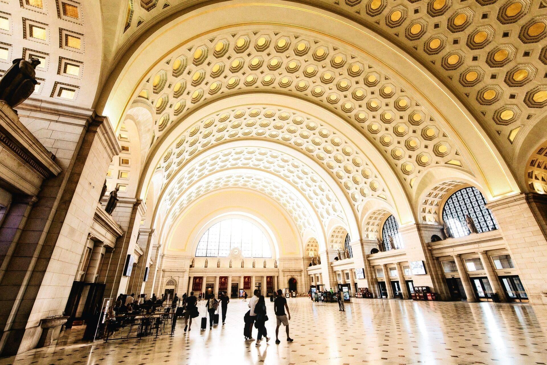 Un hall monumental avec voûtes décoratives dorées et arches concentriques, accueillant des visiteurs dans une architecture classique impressionnante