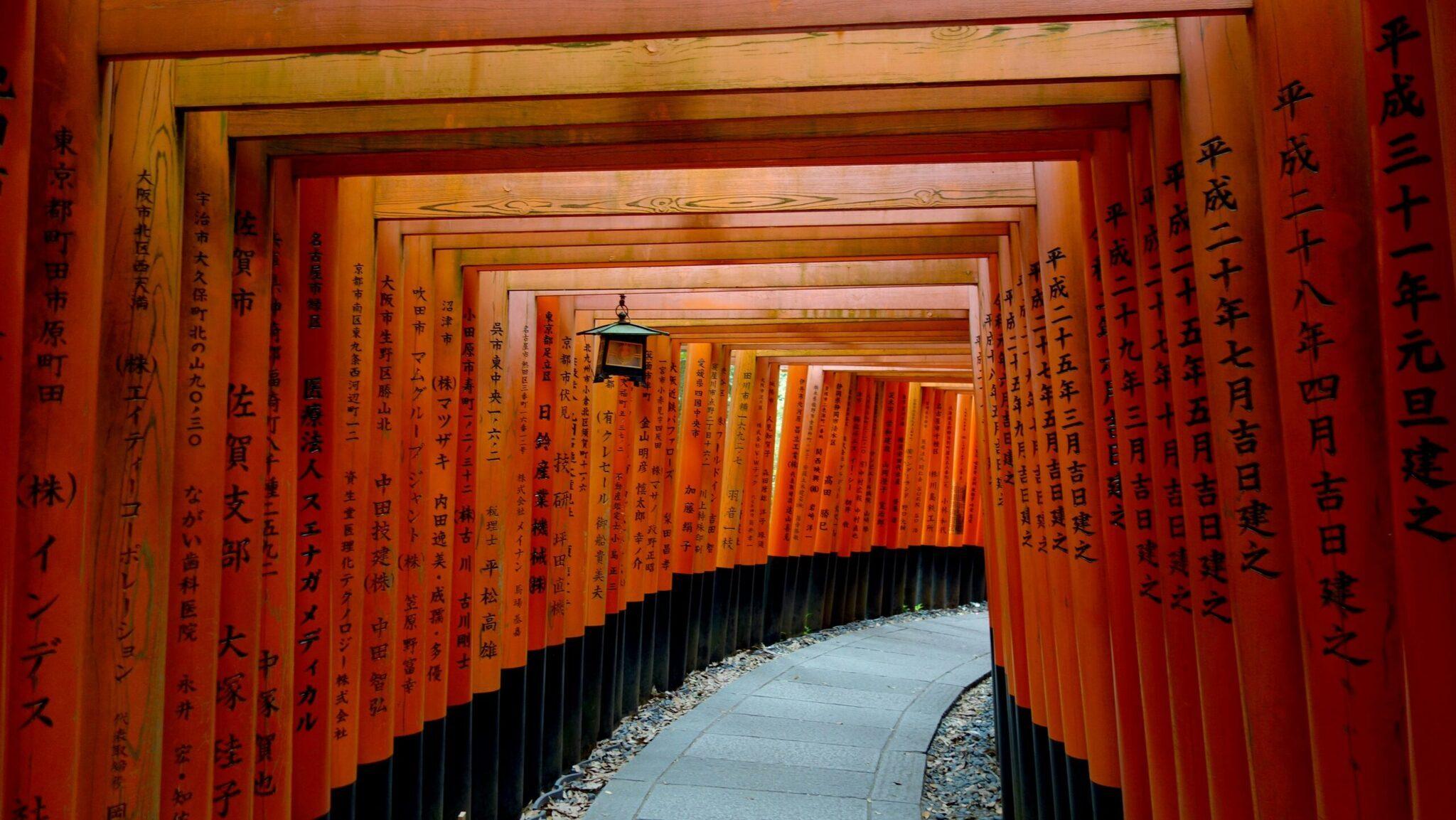 Tunnel de milliers de torii rouges avec caractères japonais dans un sanctuaire traditionnel