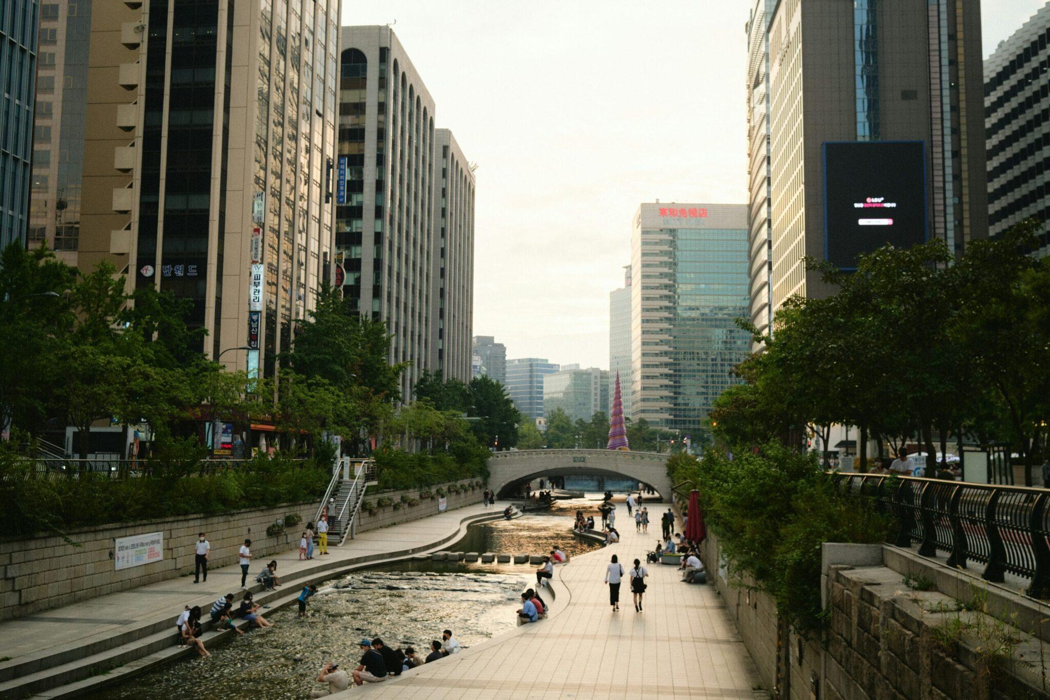 Parc urbain avec rivière aménagée, immeubles modernes et passants dans une métropole asiatique dynamique