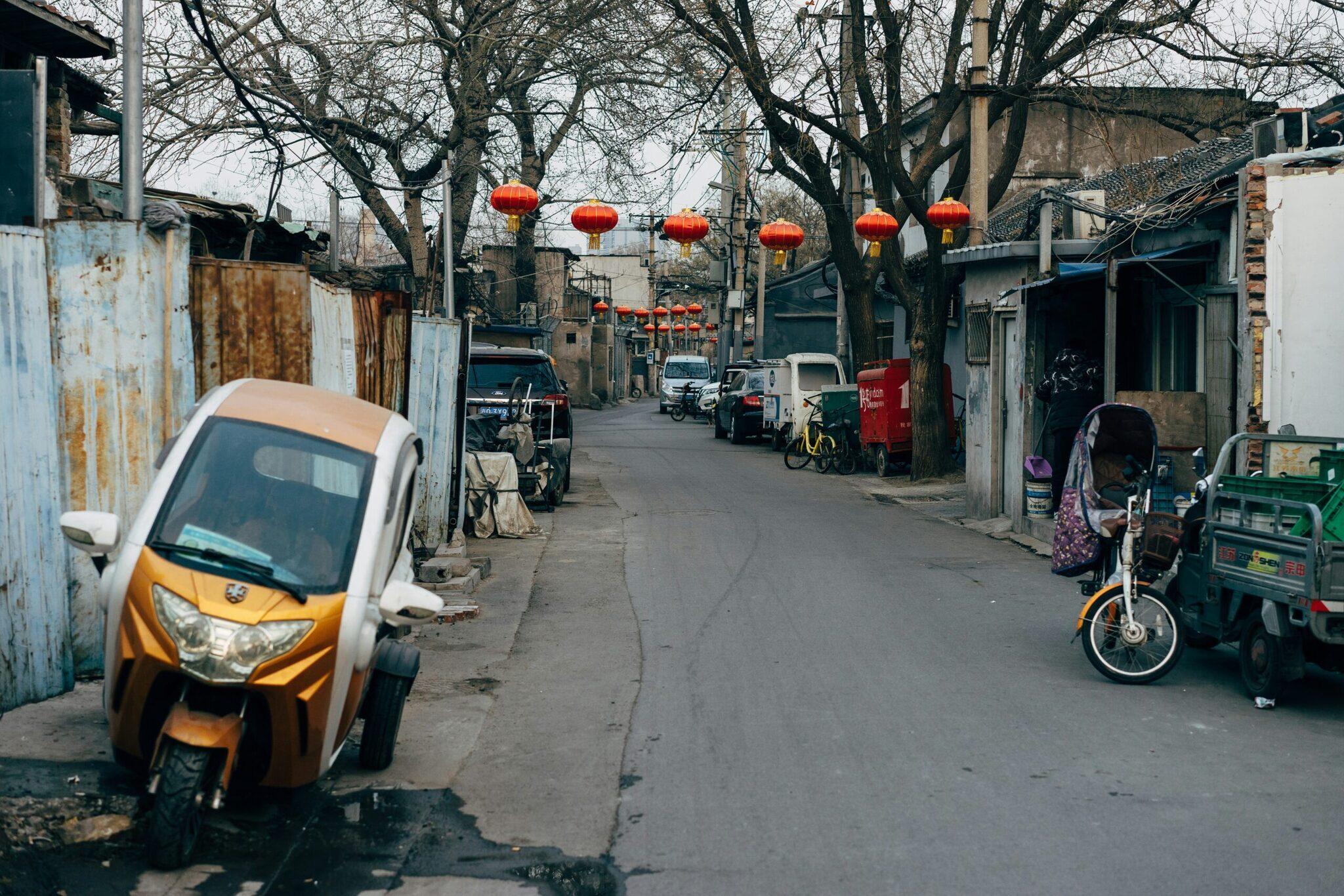 Une ruelle urbaine chinoise avec des lanternes rouges, des véhicules garés et des bâtiments résidentiels traditionnels
