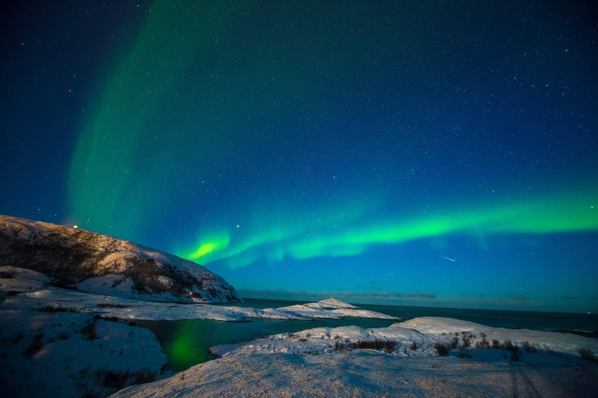 Aurores boréales vertes illuminant un ciel étoilé au-dessus de montagnes enneigées et lacs gelés