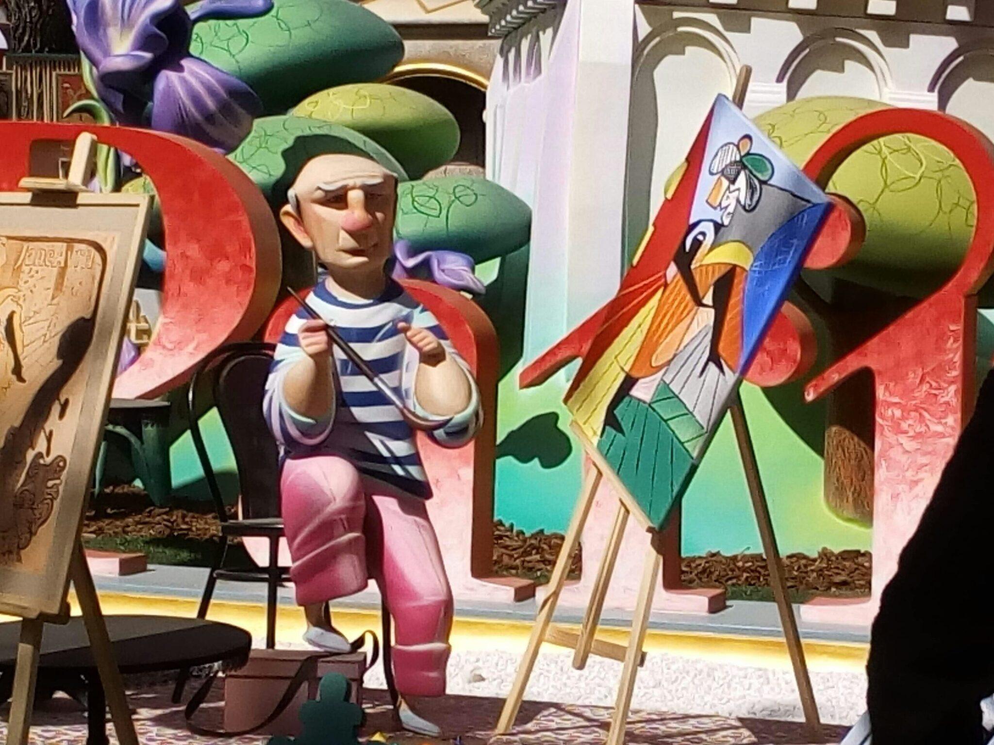 Sculpture colorée représentant un artiste peintre dans un décor urbain stylisé avec bâtiments et architecture