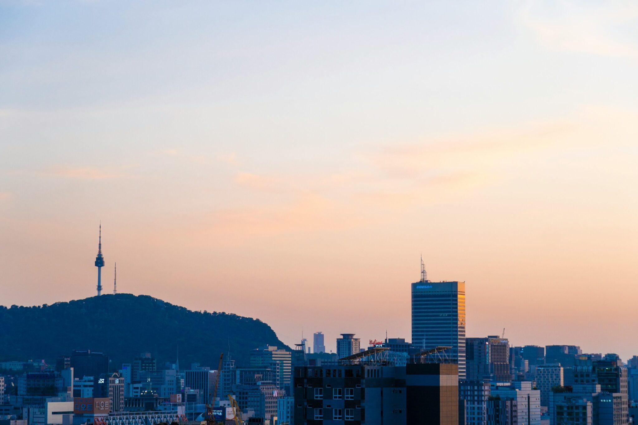 Skyline urbain au coucher du soleil avec tour de communication sur une colline boisée et gratte-ciel modernes