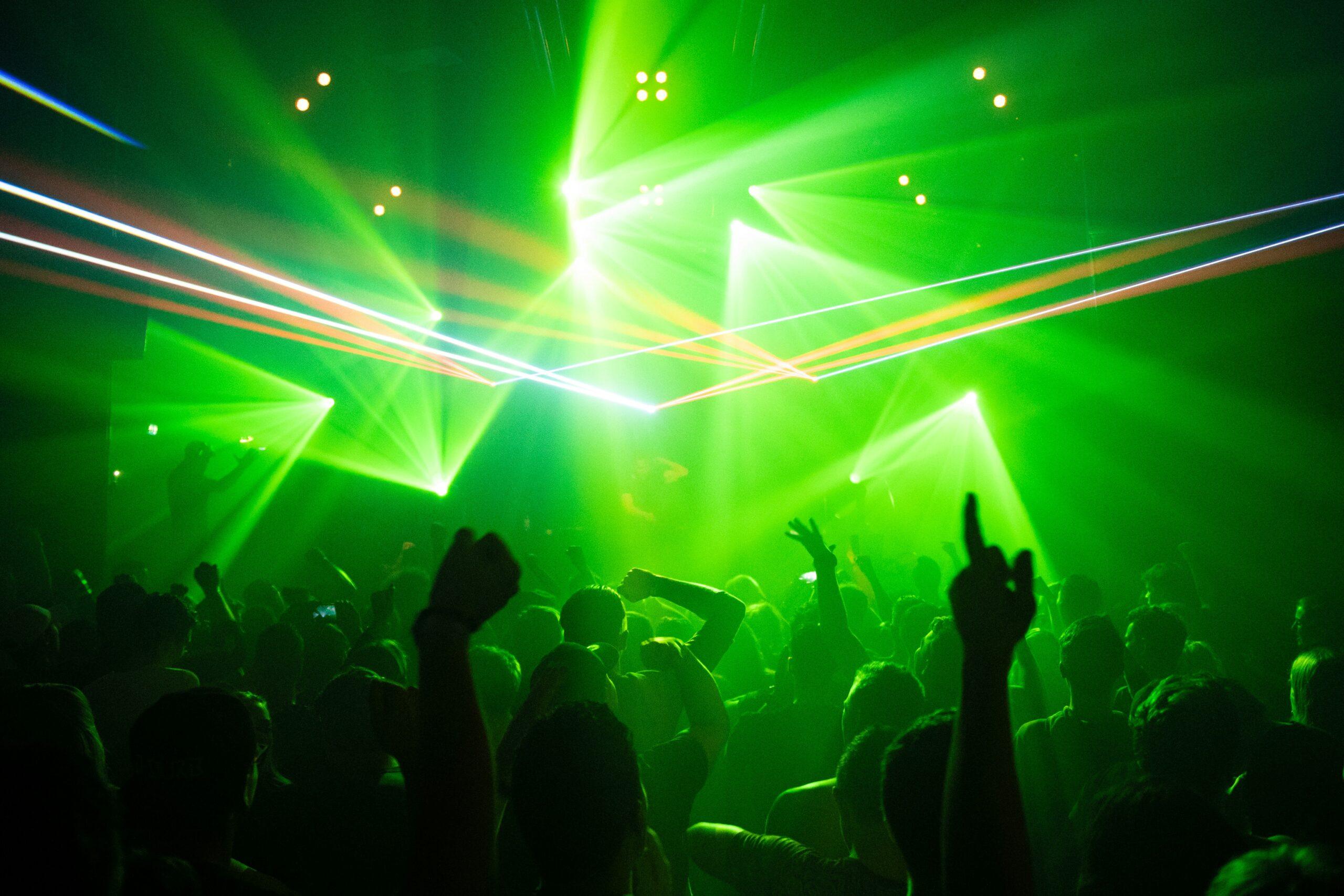 Foule de danseurs enthousiastes sous des projecteurs verts intenses dans une discothèque