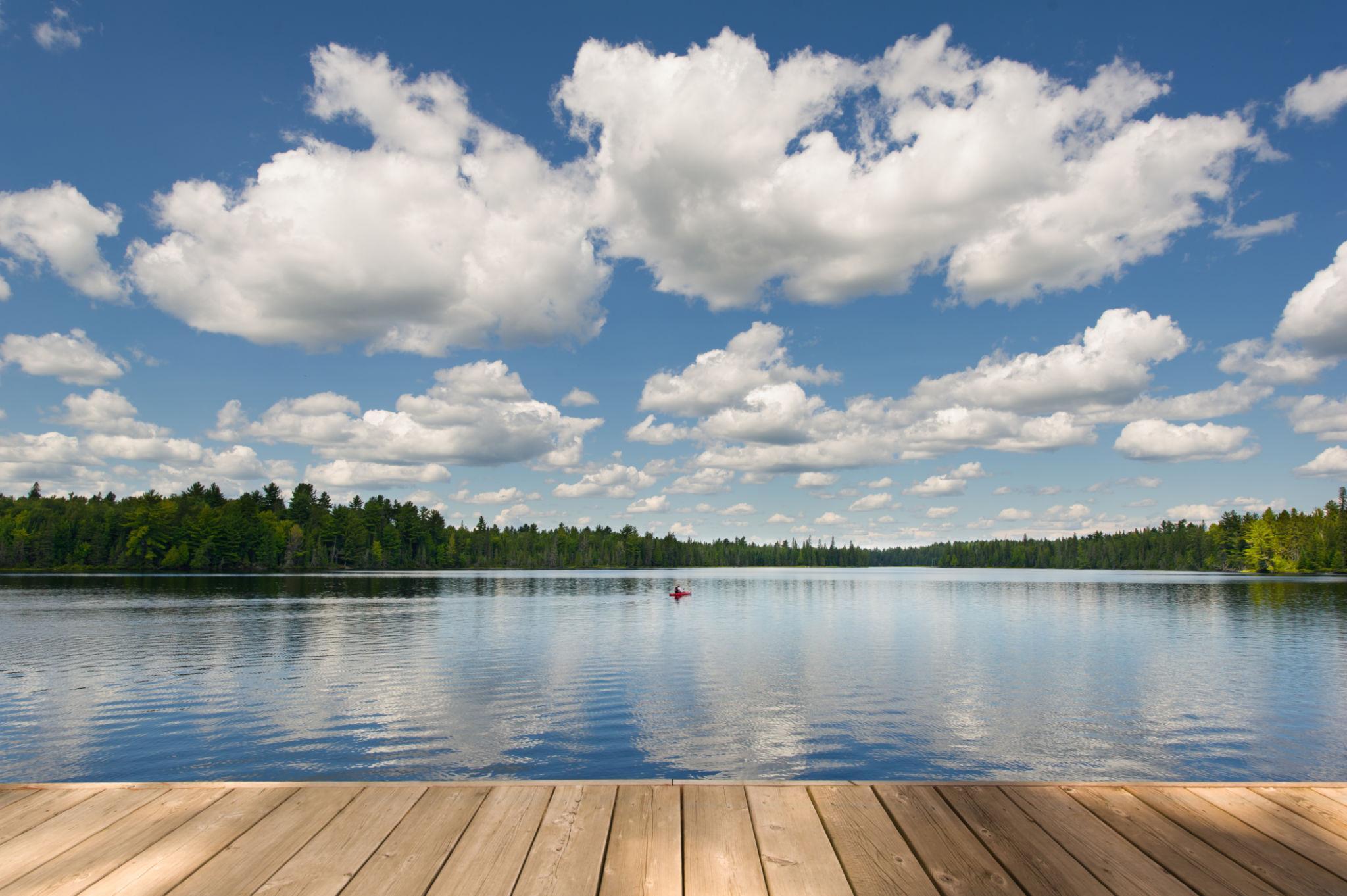 Vue depuis un quai en bois sur un lac calme bordé de forêt de conifères sous un ciel nuageux