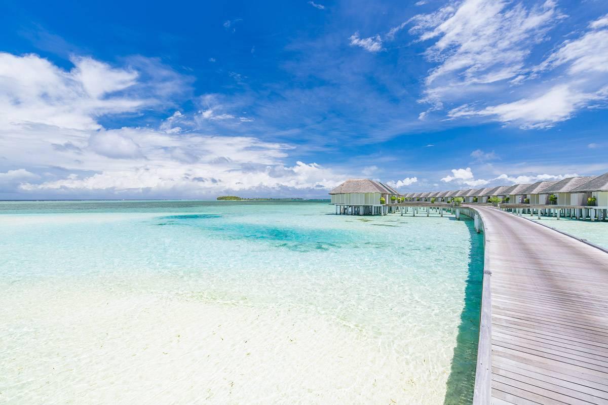 Vue aérienne d’un resort tropical avec bungalows sur pilotis, lagon turquoise cristallin et ciel bleu dégagé