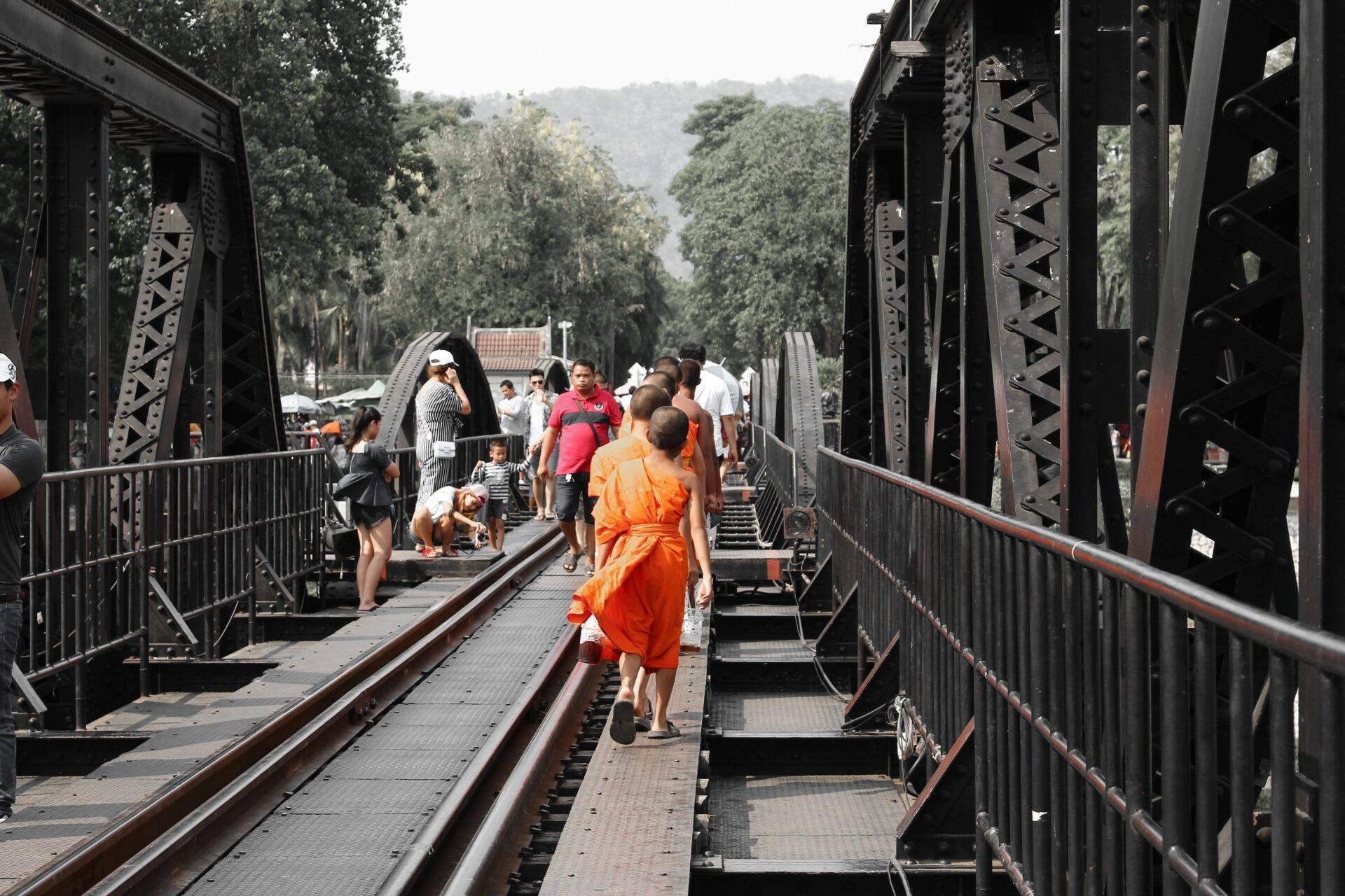 Touristes traversant un pont métallique ferroviaire en acier entre des montagnes boisées en Thaïlande