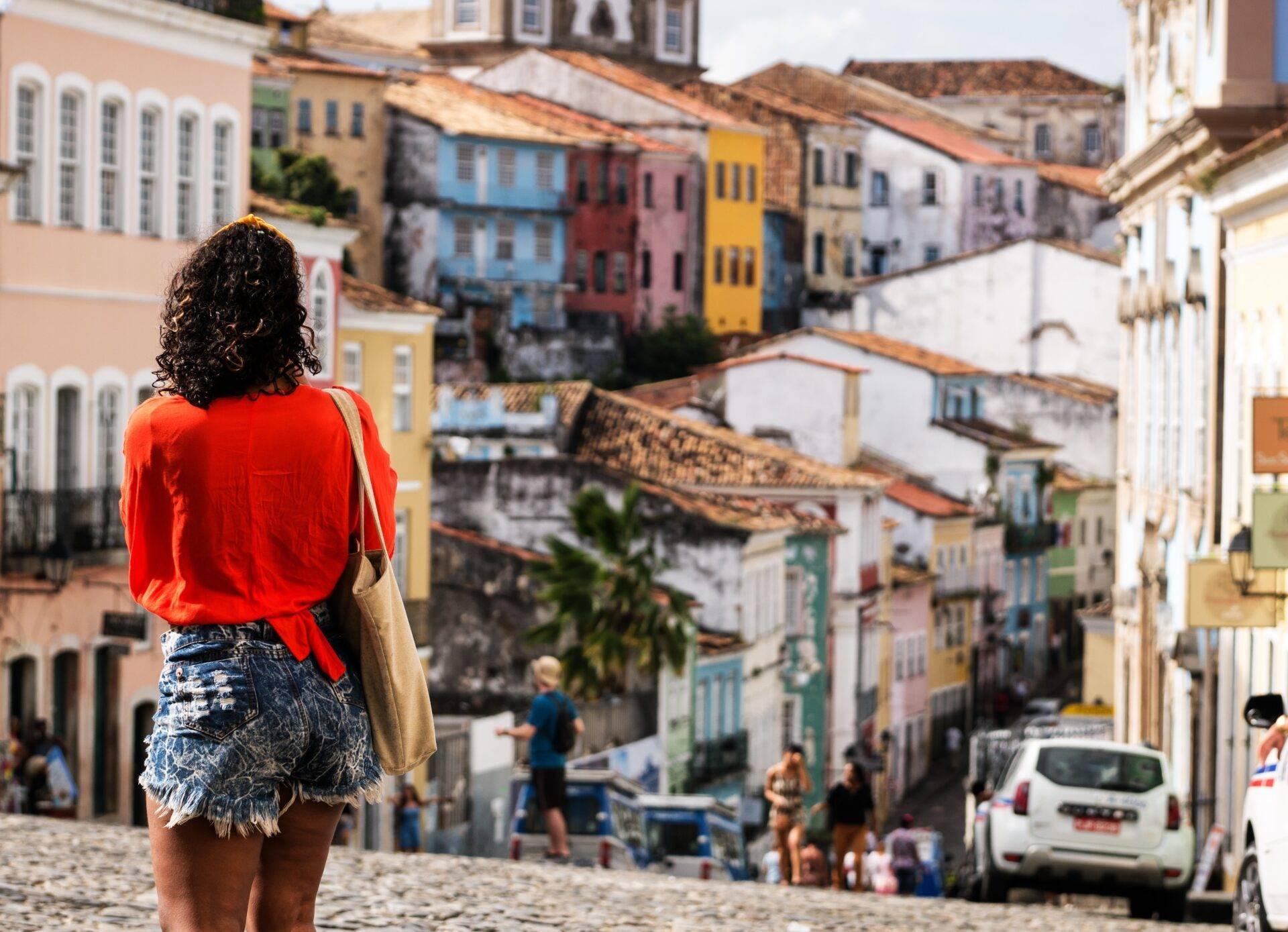 Une femme en chemise rouge observe une rue pavée colorée avec maisons coloniales traditionnelles